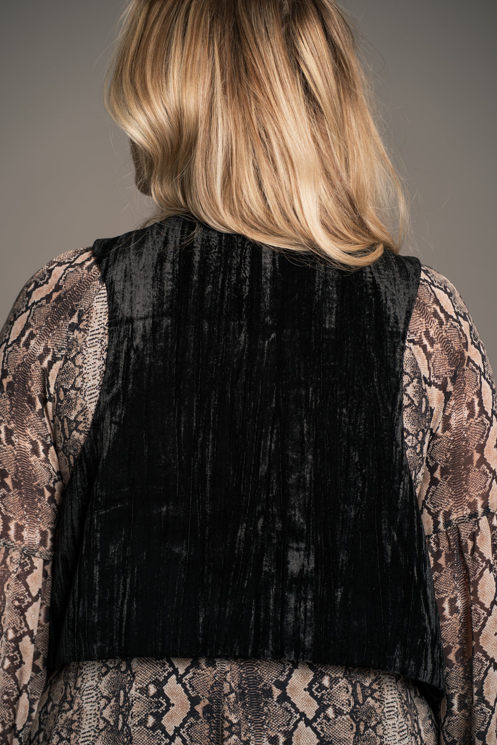 Back view of Little Lies Lennon black velvet waistcoat with cropped fit and smooth panel detailing over patterned dress