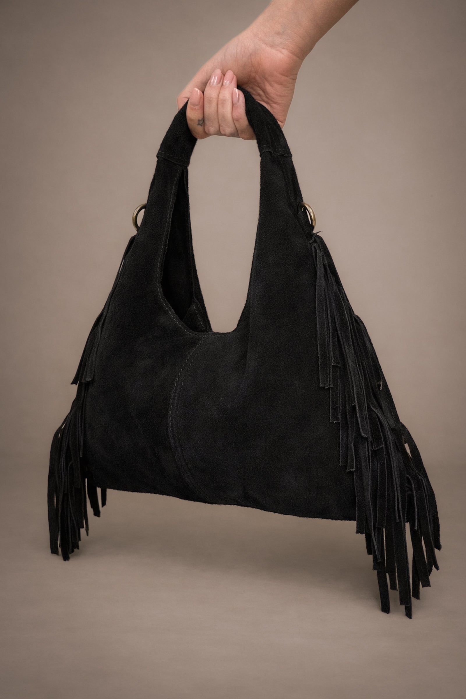 Little Lies Lila black genuine suede fringed grab bag held in studio setting.