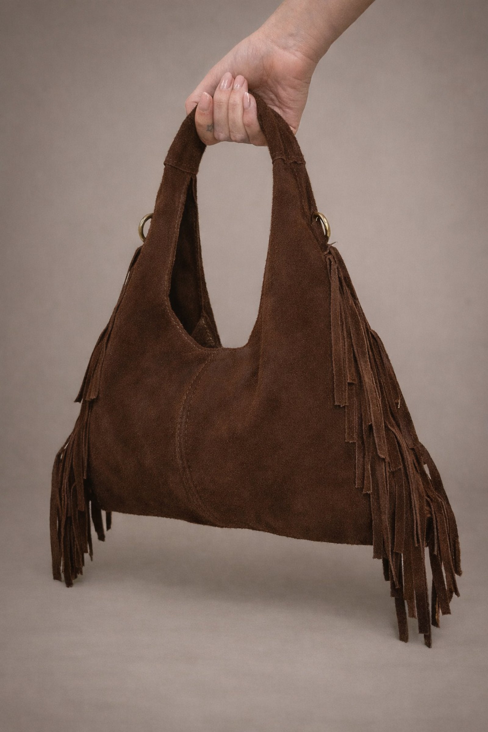 Little Lies Lila chocolate genuine suede fringed grab bag held in studio setting.