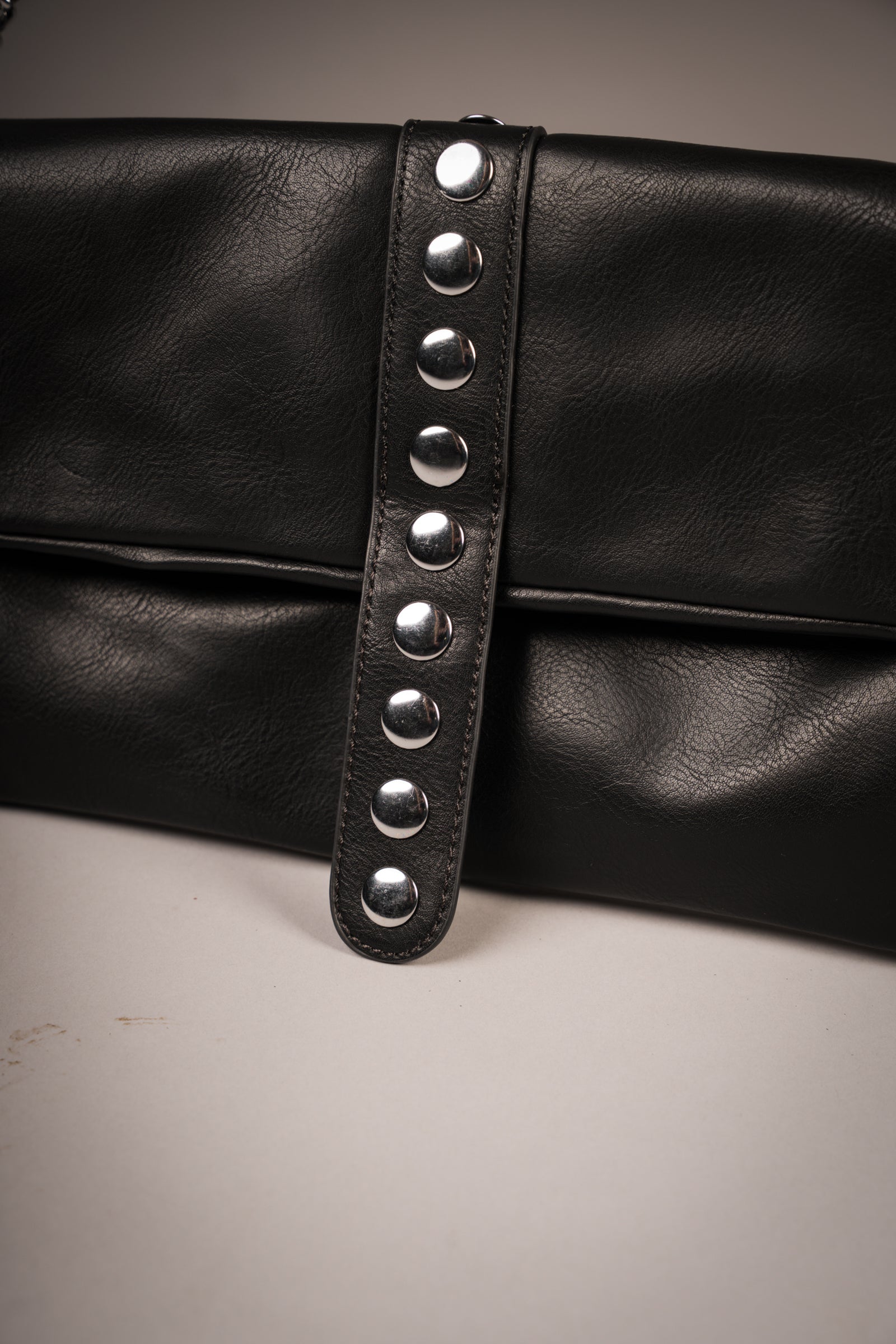 Close-up of Little Lies Zoë studded black faux leather clutch showing silver-tone stud detailing on front strap, studio setting