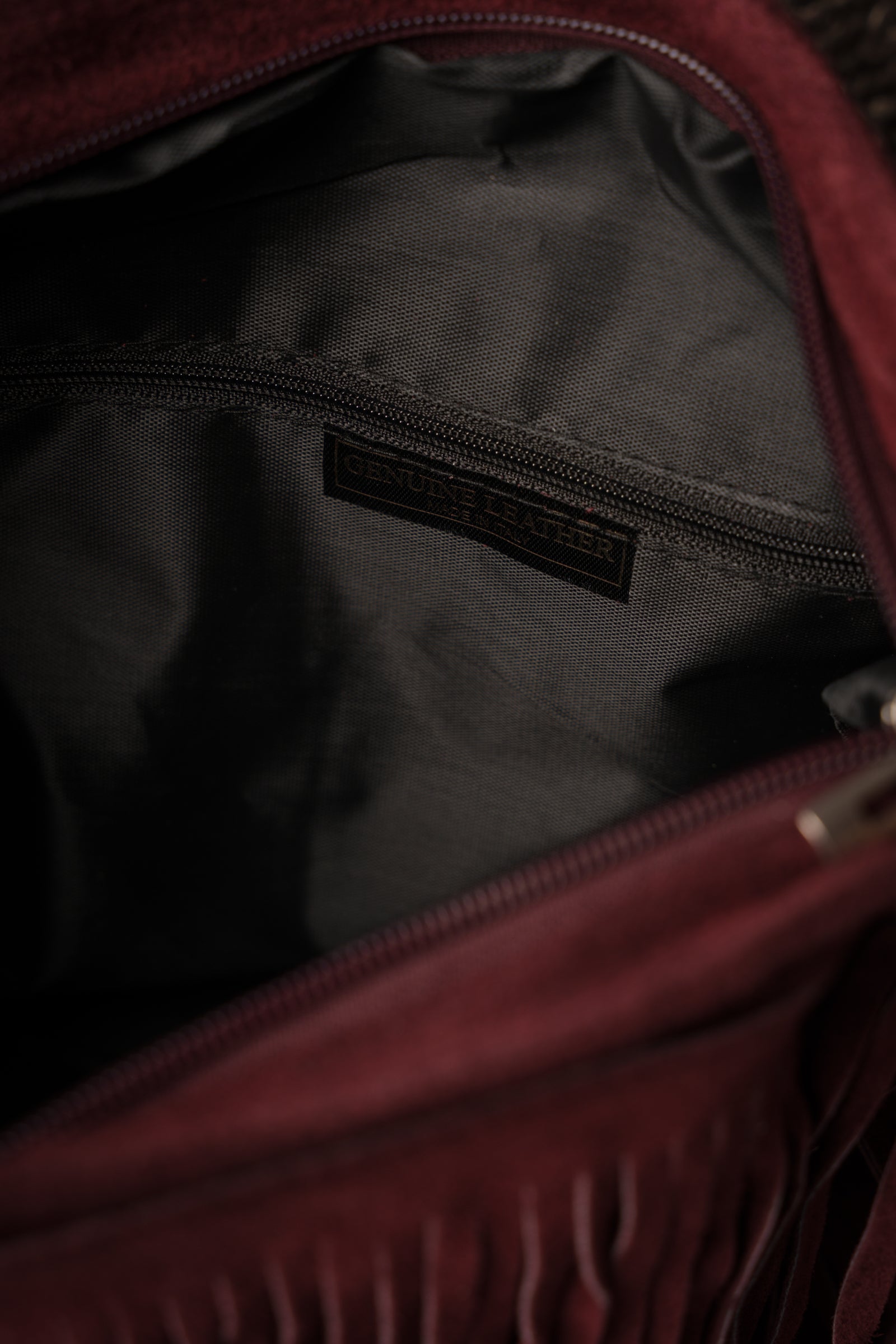 Close-up of interior of Little Lies Oxblood Genuine Suede Fringed Bag showing black fabric lining and zip pocket with Genuine Leather label