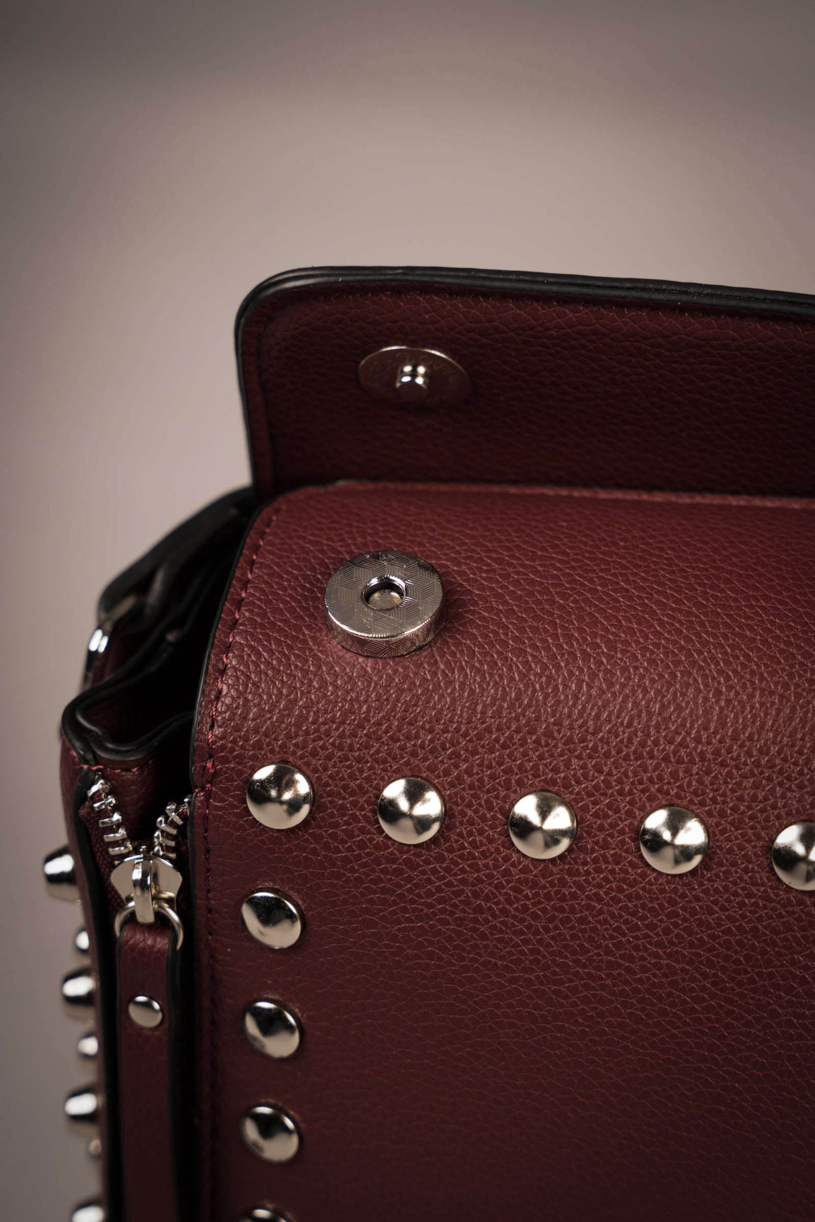 Little Lies Leo Burgundy studded box bag close-up showing zip detail, silver studs, and magnetic snap opening
