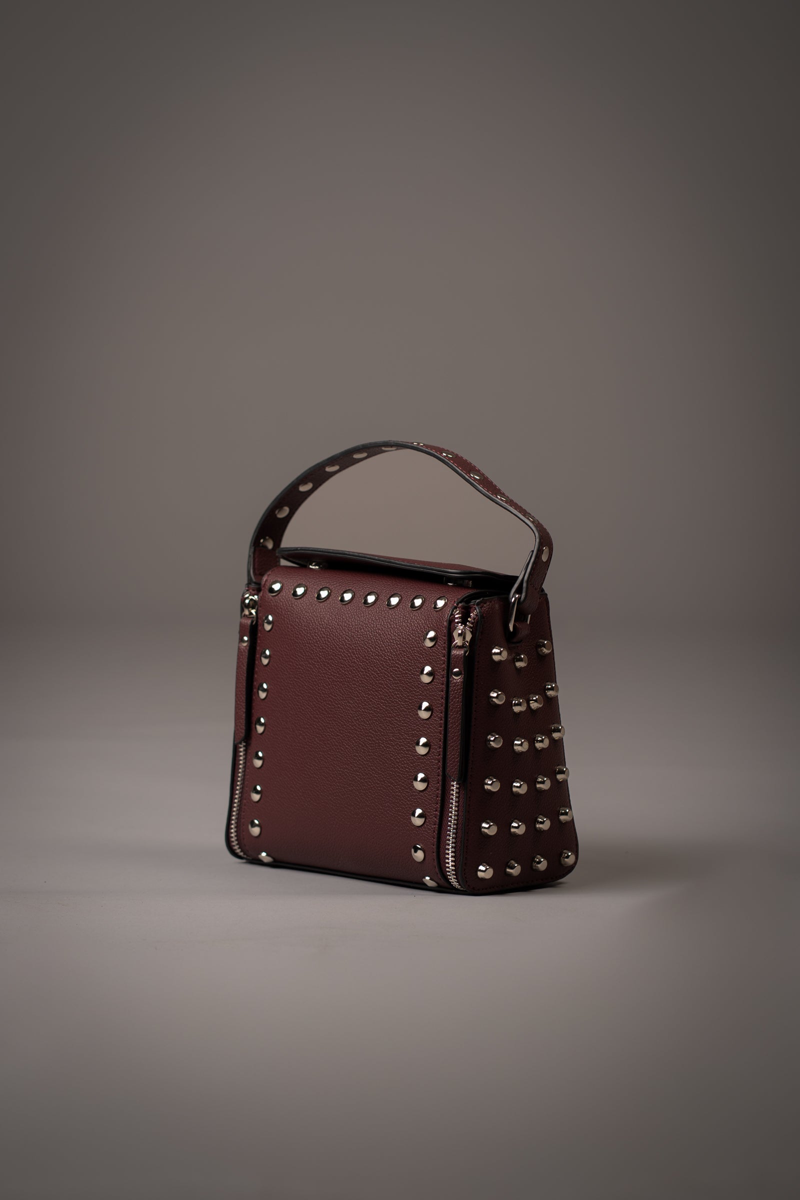 Little Lies Leo Burgundy Studded Box Bag with, zip features, silver hardware and short handle detail, studio setting.