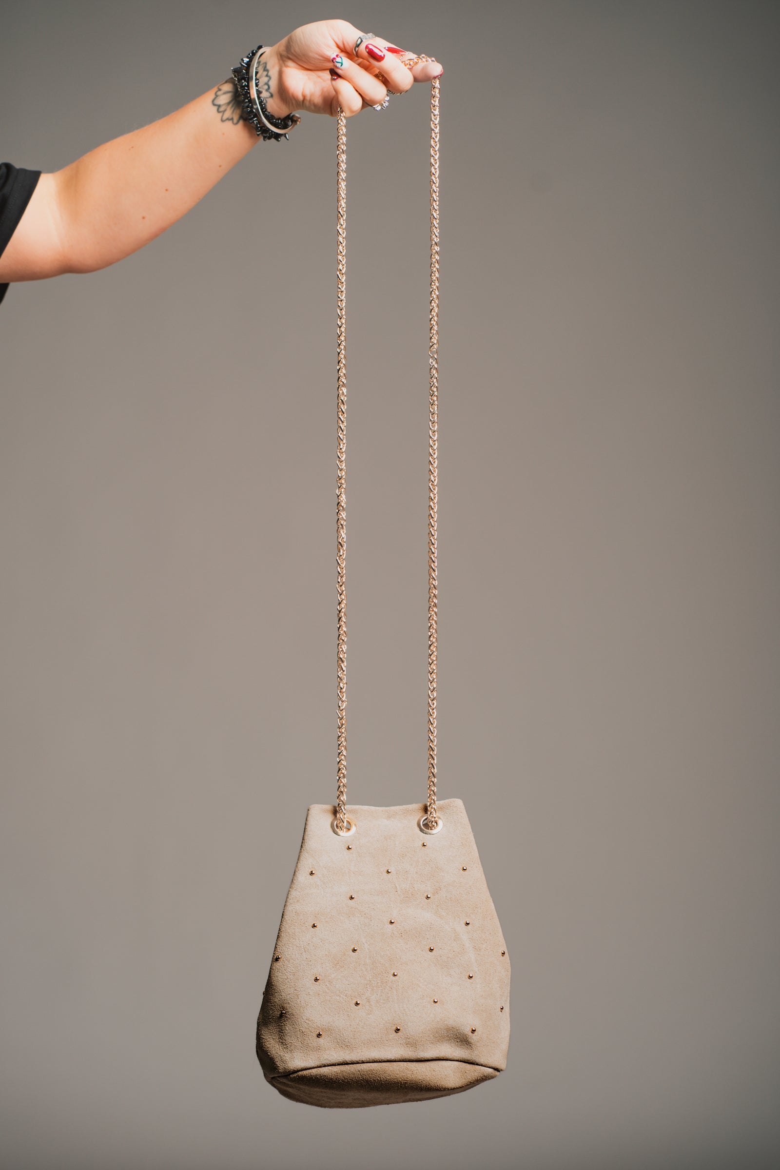 Model carrying the Lola Genuine Suede Studded Bucket Bag with a dark background