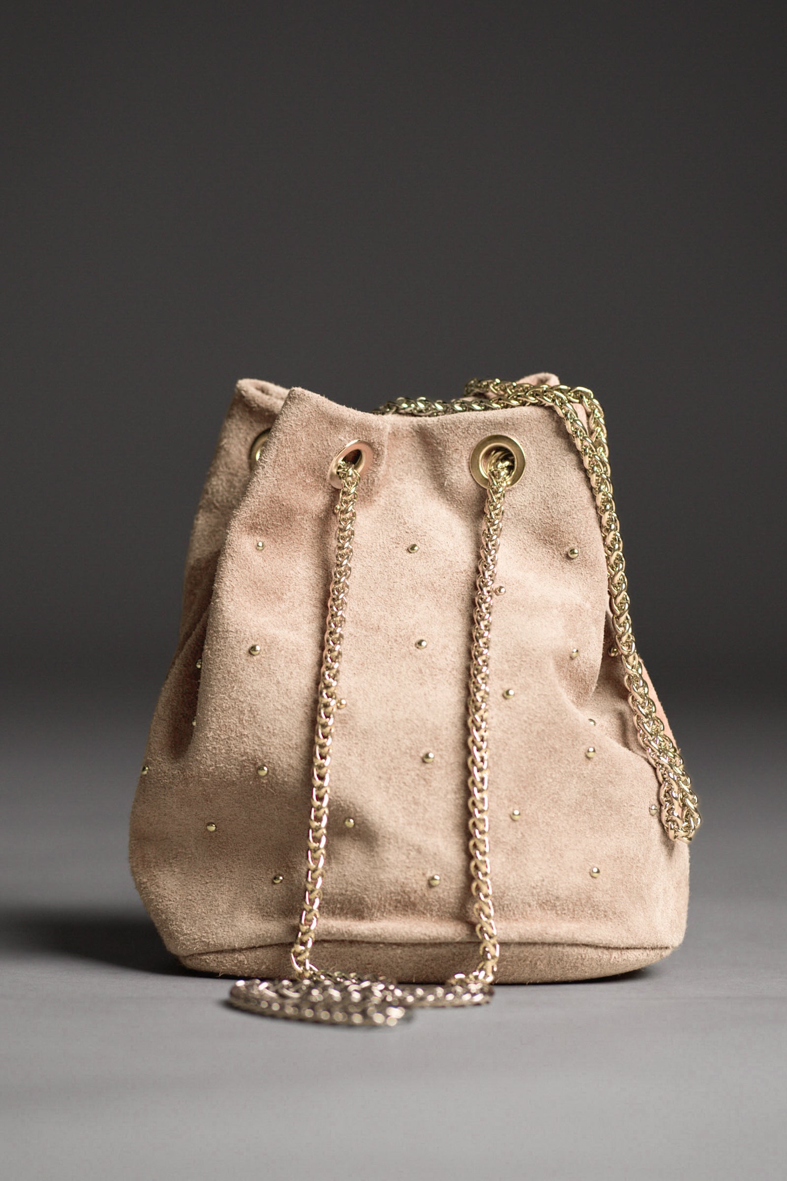 Model carrying the Lola Genuine Suede Studded Bucket Bag with a dark background