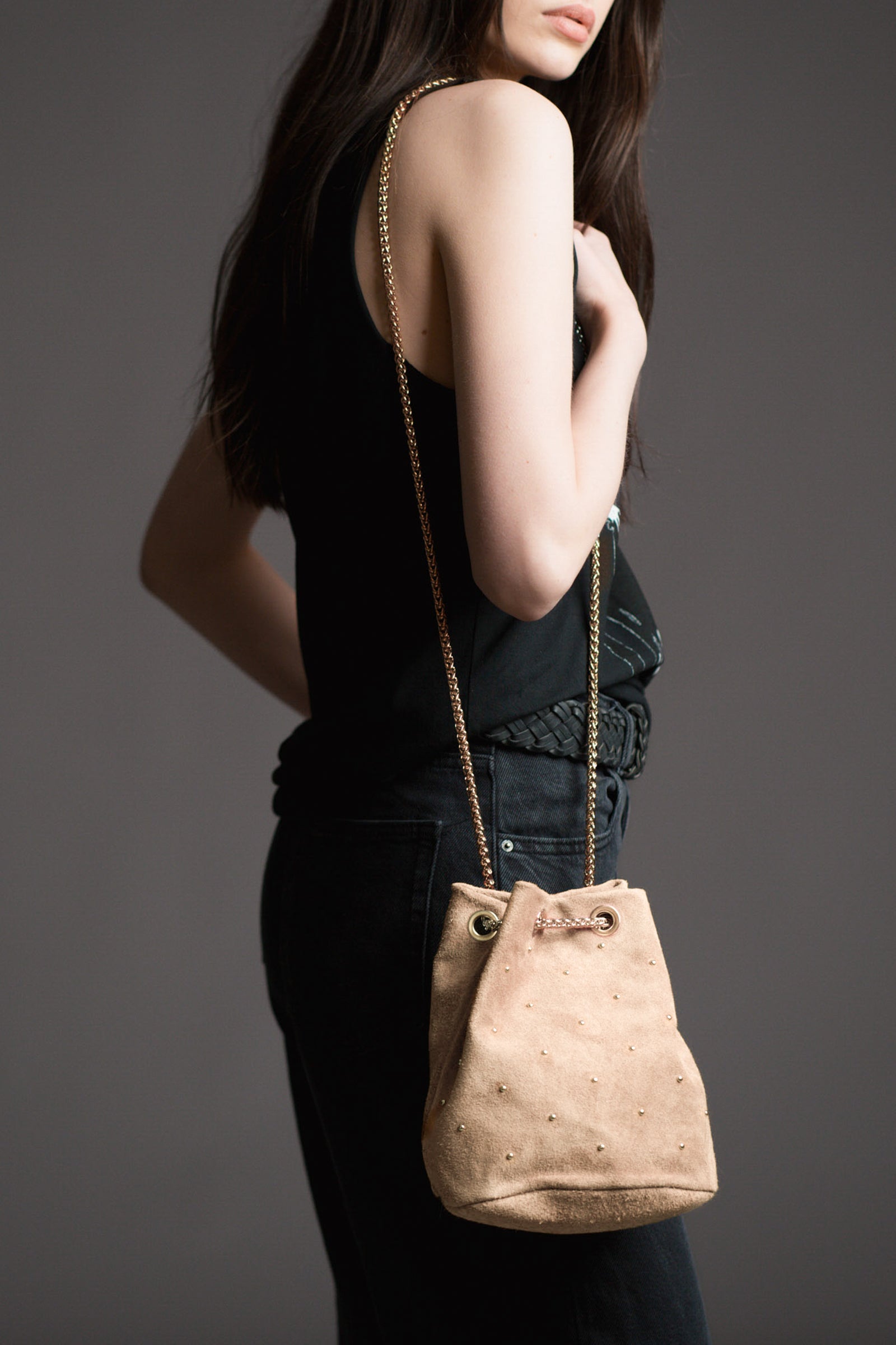 Model carrying the Lola Genuine Suede Studded Bucket Bag with a dark background