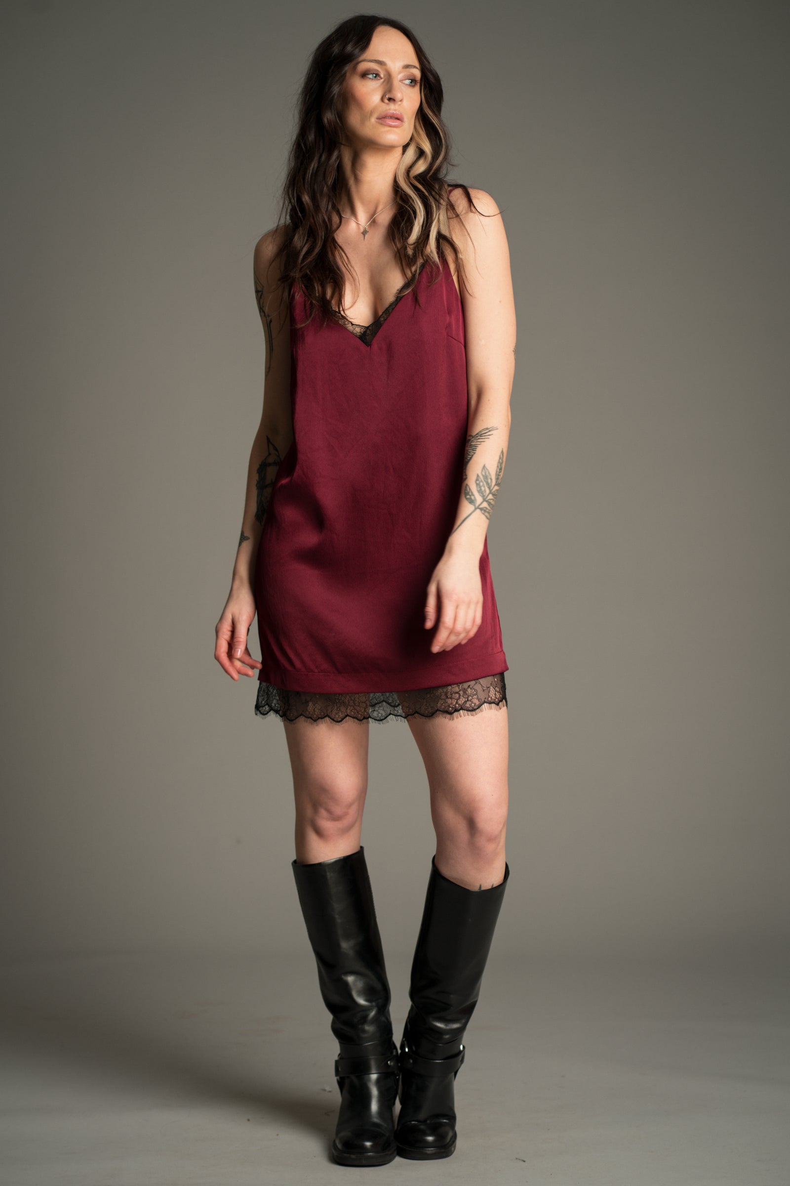 Victoria posing in plum Nightbird Satin mini dress with lace trim and black knee high boots