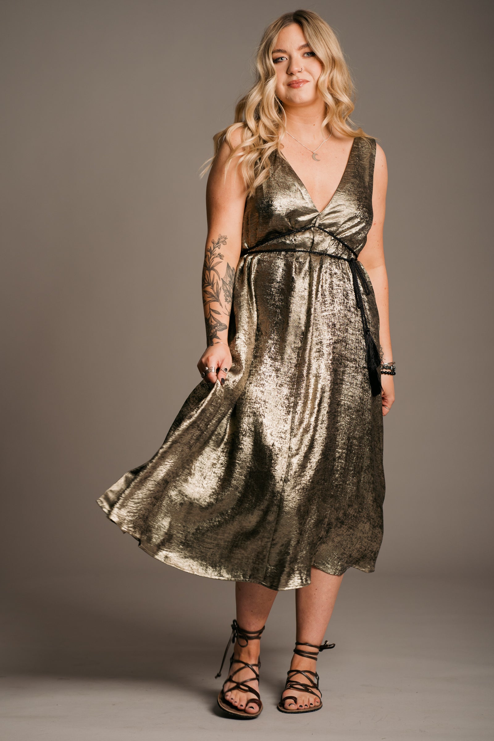 Blonde model in front of a grey backdrop in studio. Erin is wearing the Little Lies Ramble on Gold metallic Midi Dress, tie sandals and Little Lies Crescent Moon Necklace
