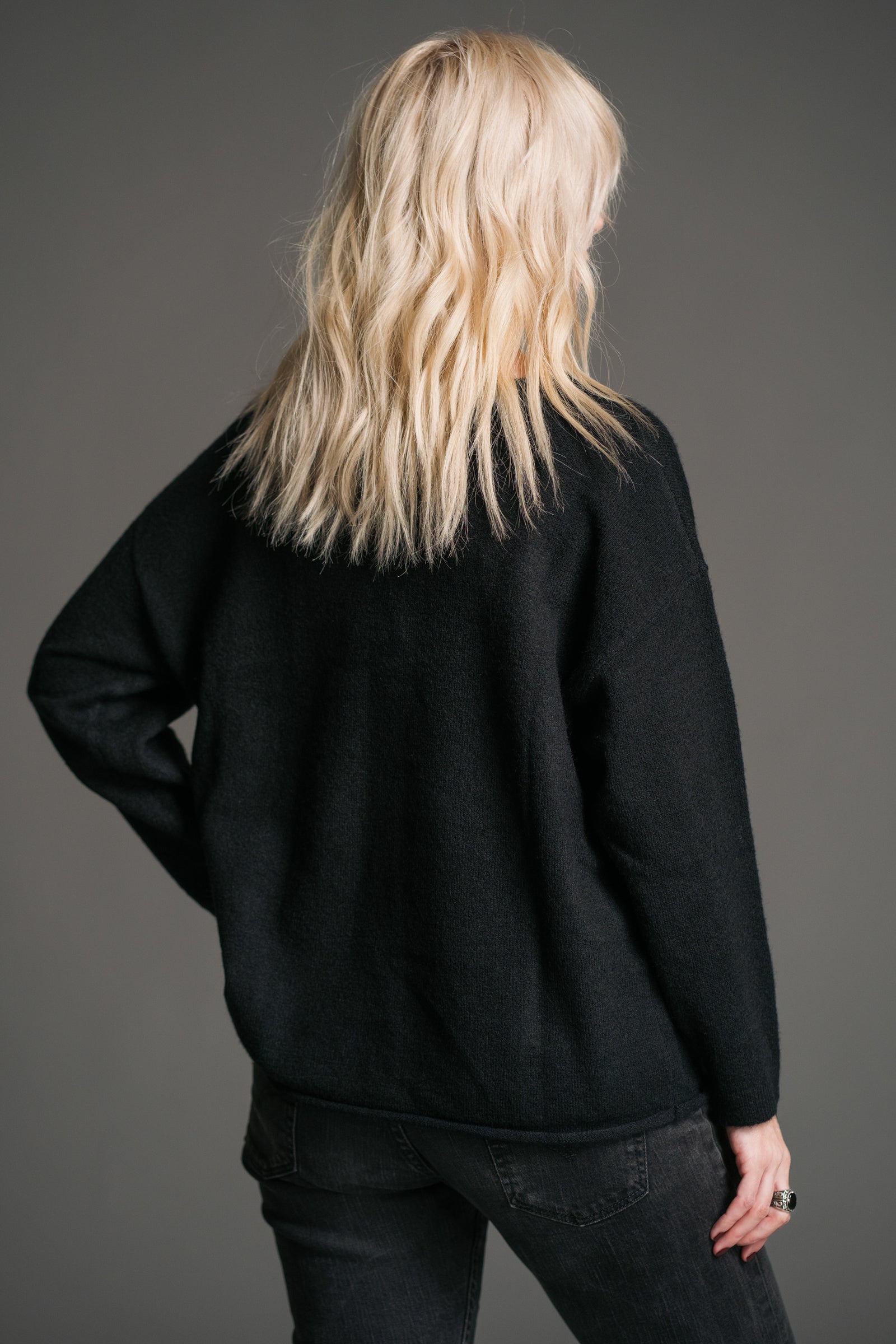 Sara showing the back of the Rebel Rebel Black Graphic Jumper on a gray background
