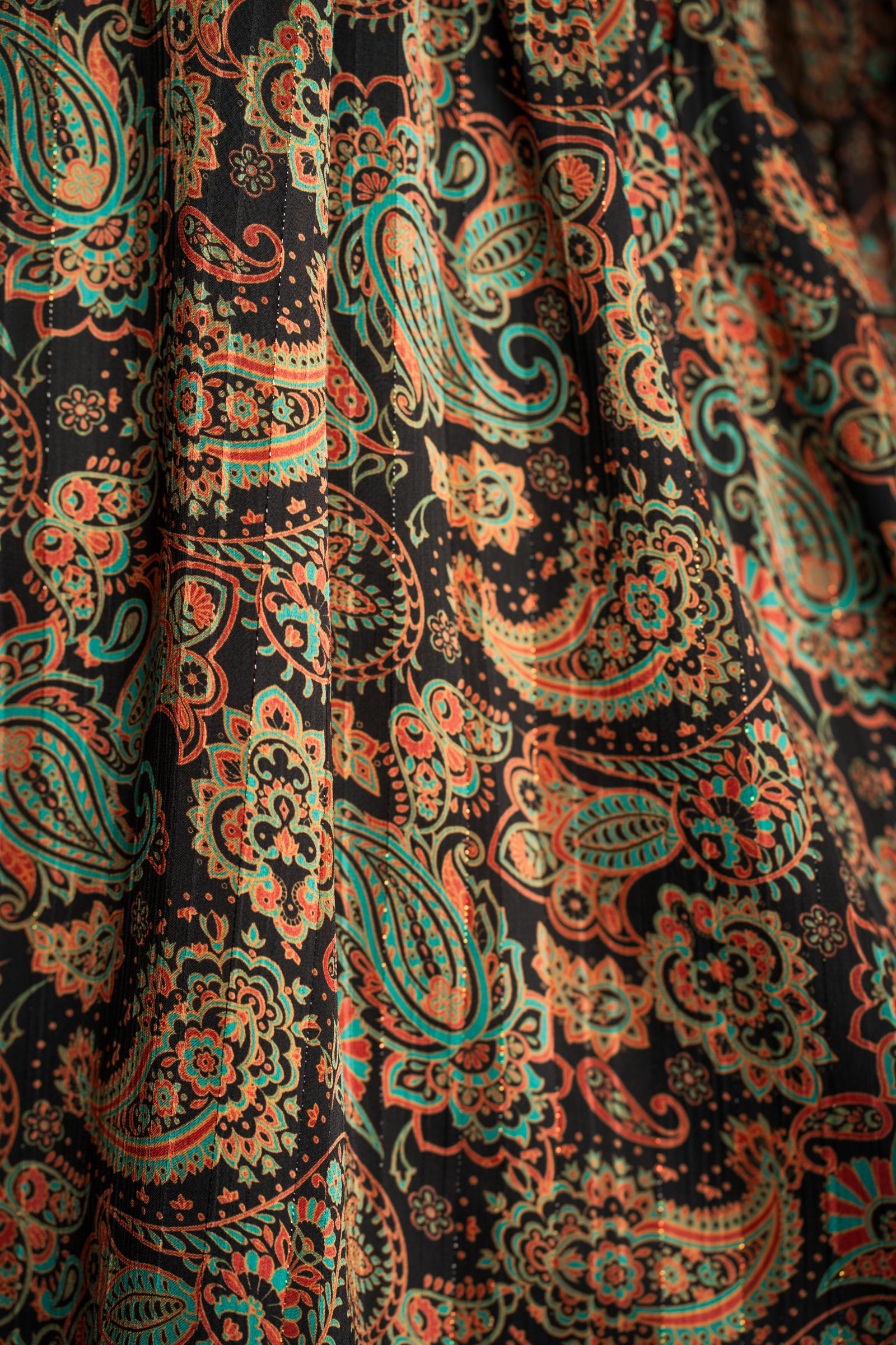 Close-up of Little Lies Ringo dress fabric showing intricate green, gold and rust paisley pattern on soft black base