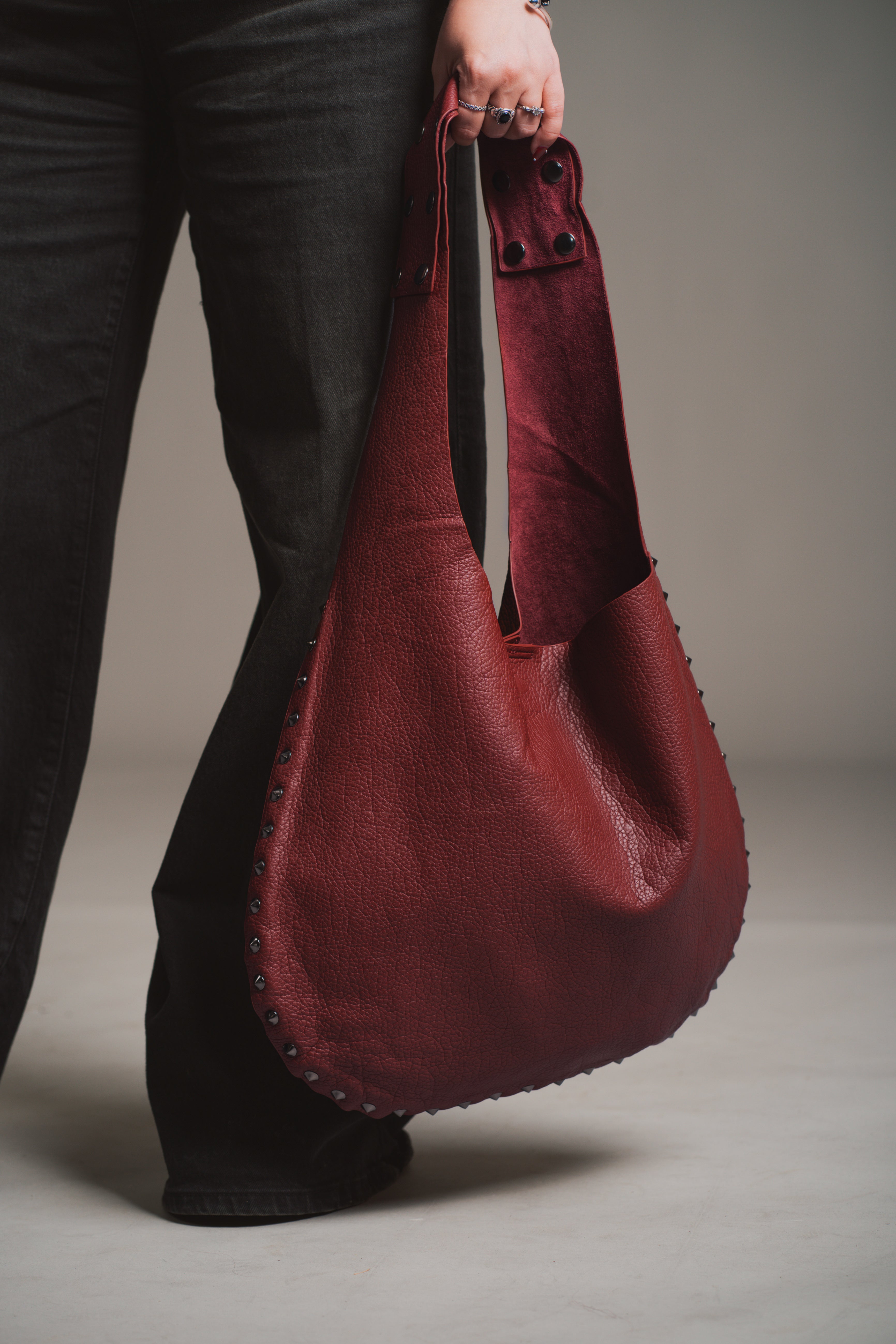 Model holding the Romy Studded Faux Leather Hobo Bag against a gray background