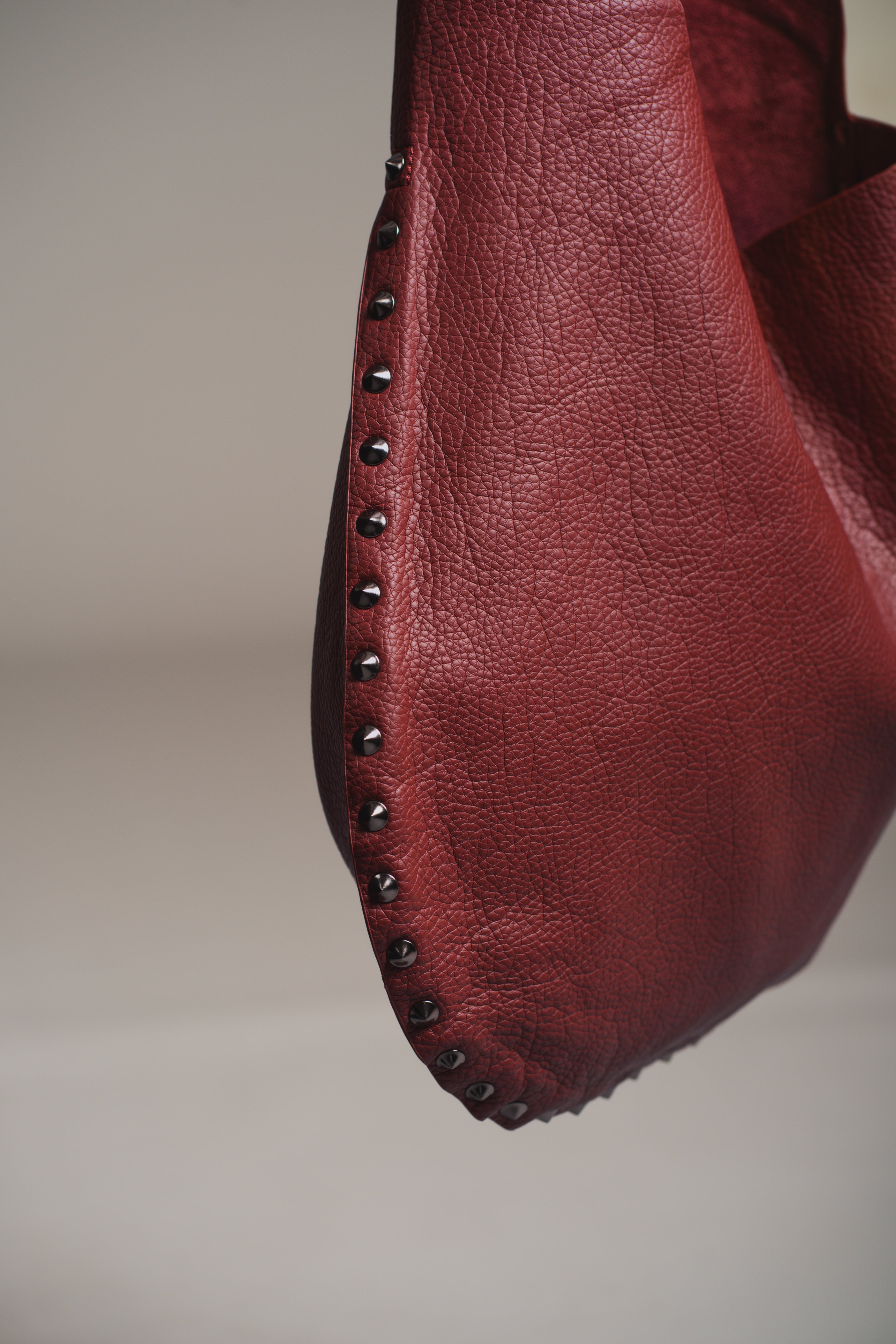 Model holding the Romy Studded Faux Leather Hobo Bag showing stud detail against a gray background