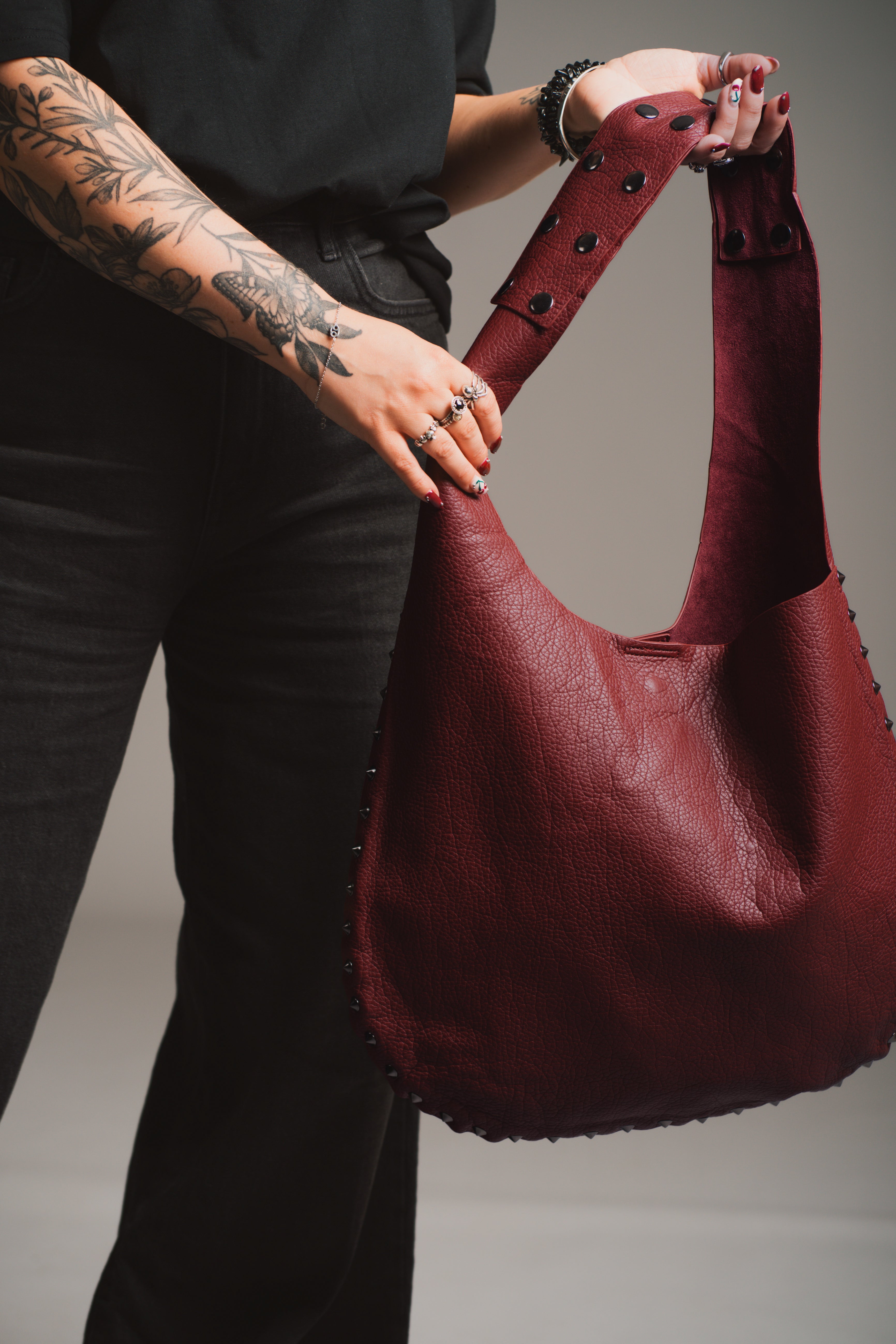 Model holding the Romy Studded Faux Leather Hobo Bag  styled with 'Rebel Rebel' tee against a gray background