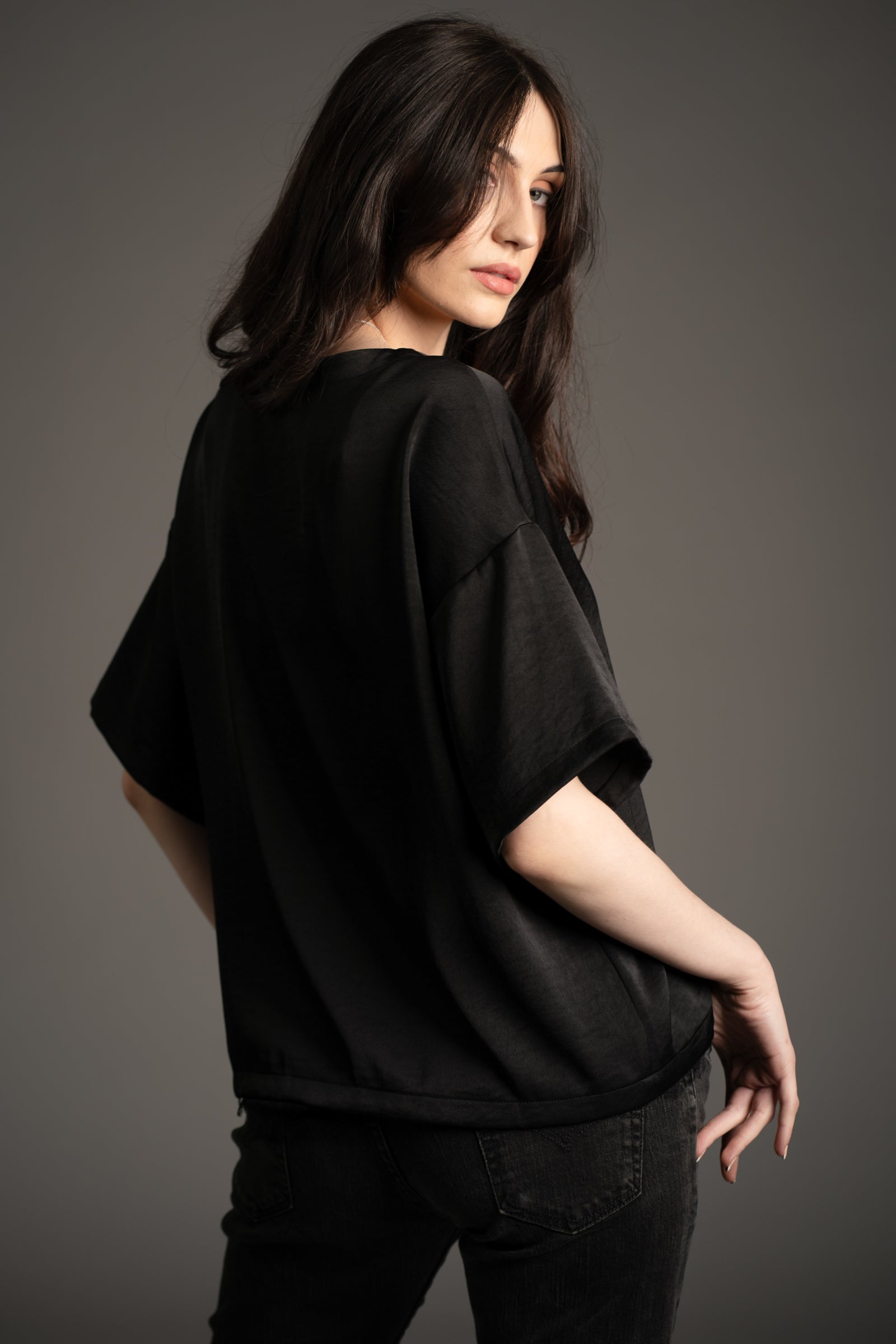 Little Lies Roxy lace trim satin tee in black, back view showing relaxed fit and short sleeves, styled with black jeans in studio setting