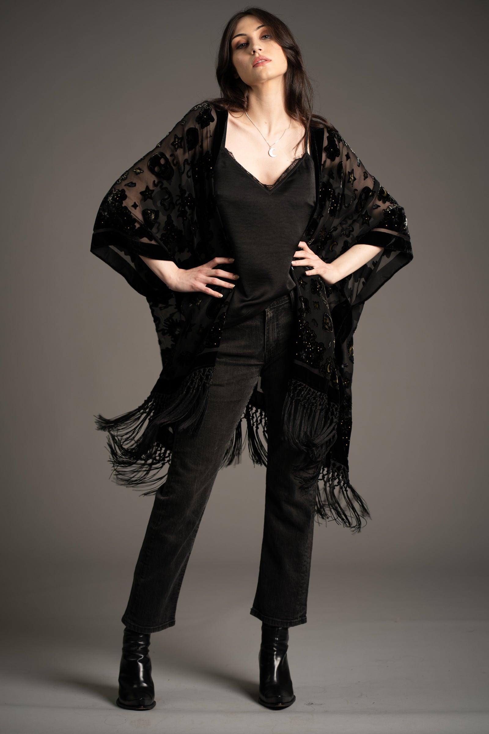 Andie models Little Lies Suzi Skull devore kimono in black with skull pattern and fringe hem, styled over black camisole and dark jeans with ankle boots in studio setting