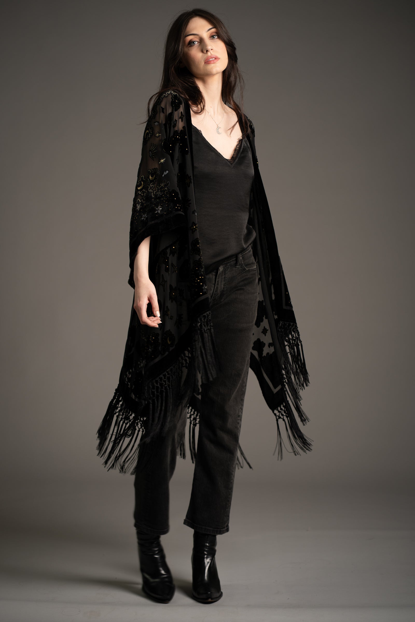Andie models Little Lies Suzi Skull devore kimono in black with skull and celestial pattern, sheer fabric and fringe hem, styled over black camisole and dark jeans with ankle boots in studio setting