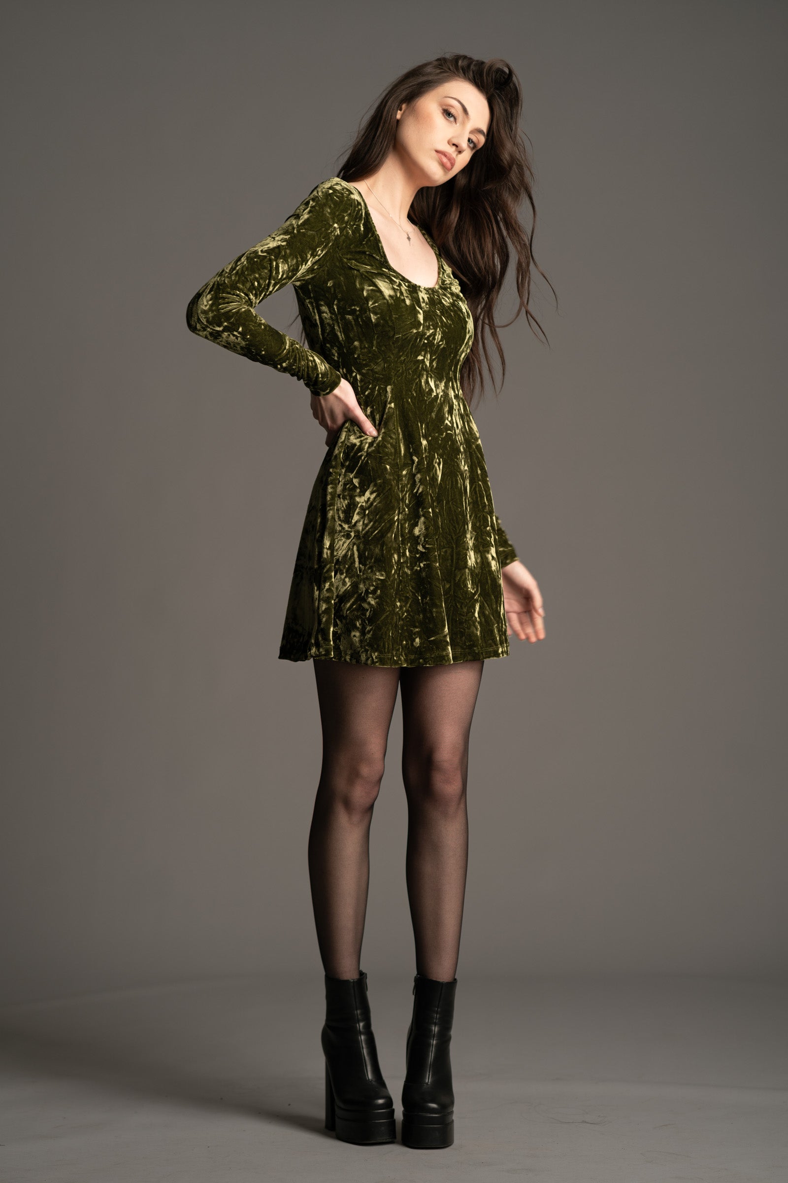 Andie wearing the Sweet Jane olive crushed velvet mini dress As worn by Taylor Swift, with long sleeves and a scoop neckline.