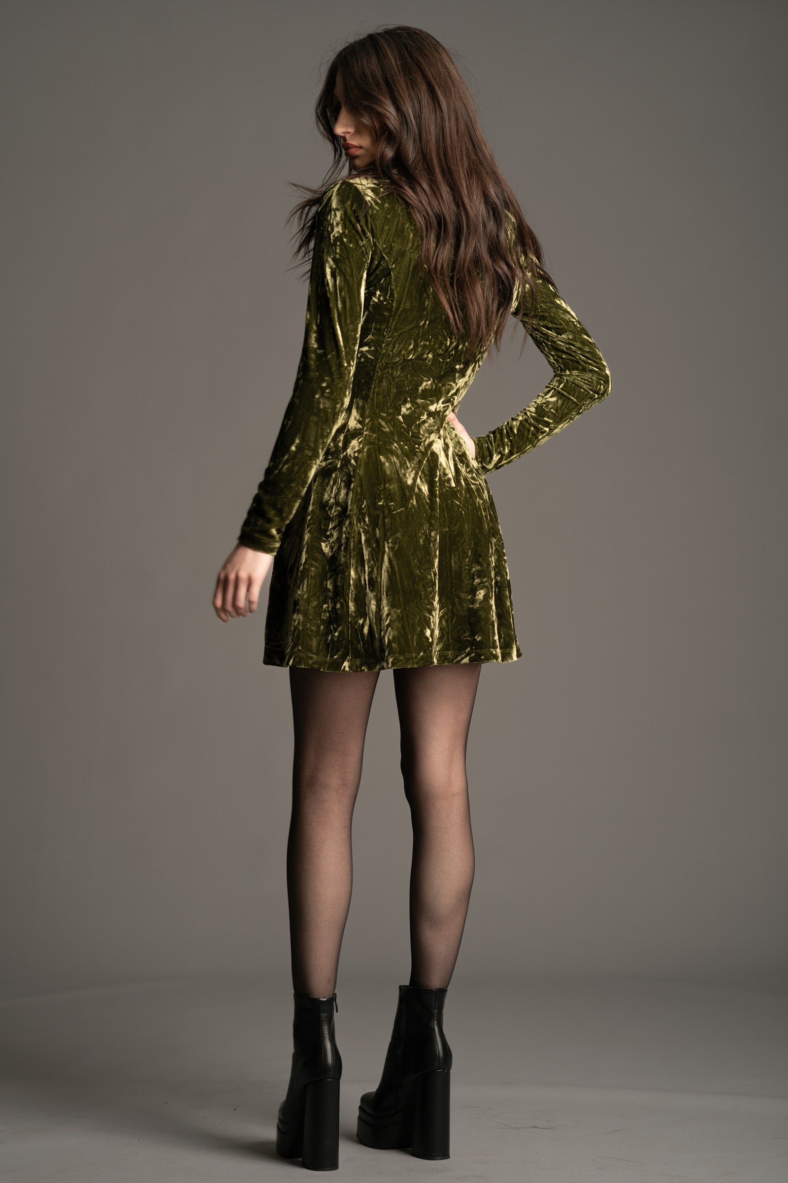 Andie wearing the Sweet Jane olive crushed velvet mini dress As worn by Taylor Swift, with long sleeves and a scoop neckline.