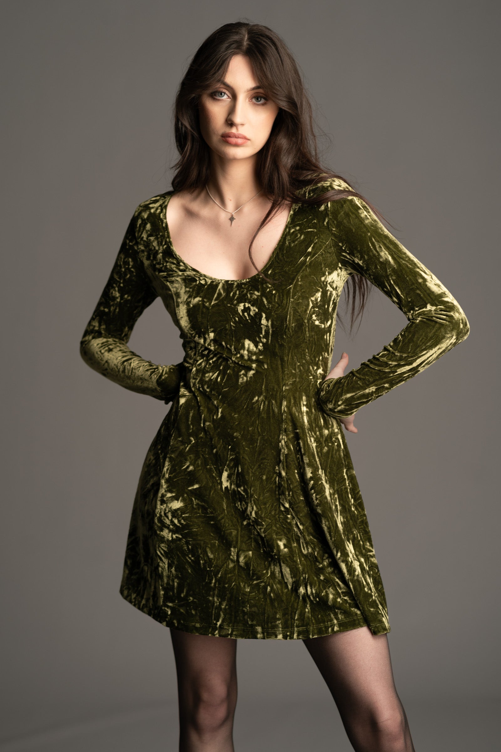 Andie wearing the Sweet Jane olive crushed velvet mini dress As worn by Taylor Swift, with long sleeves and a scoop neckline.