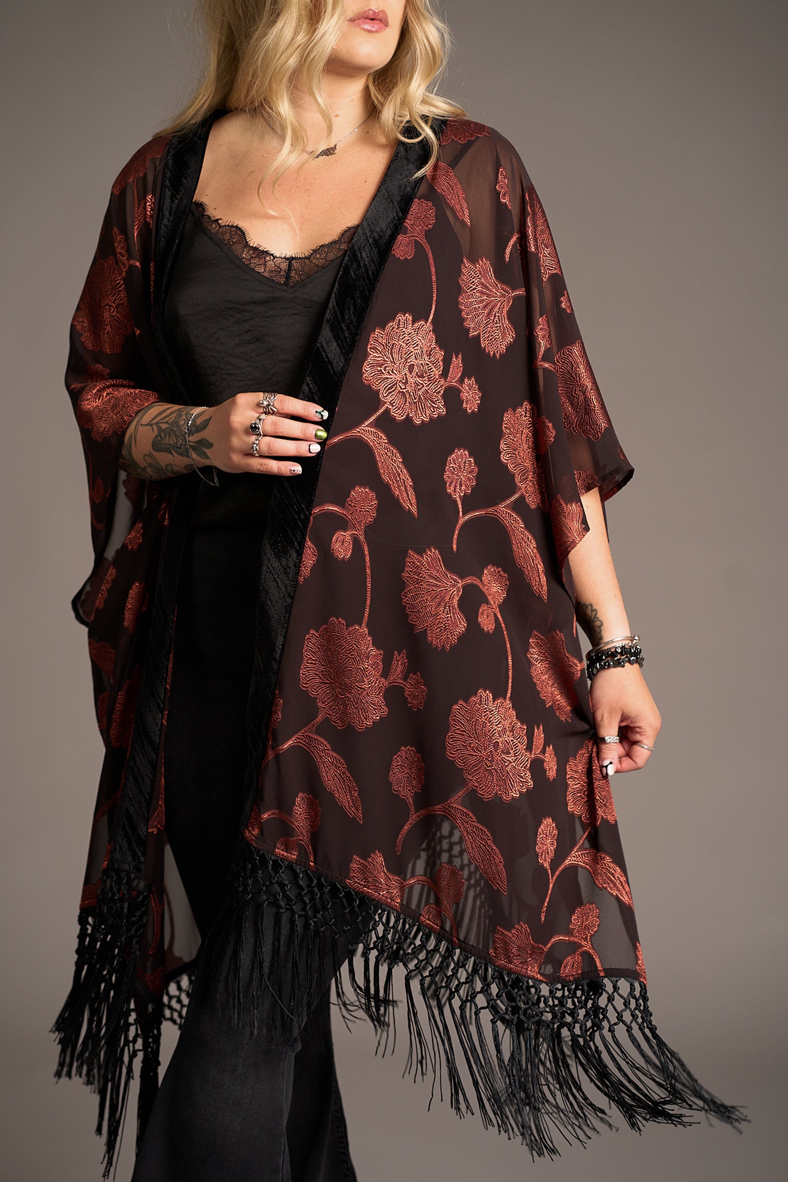 Close up of Erin showcasing the Venus Fringed Kimono in black sheer fabric with red floral print and velvet trim, over black lace top