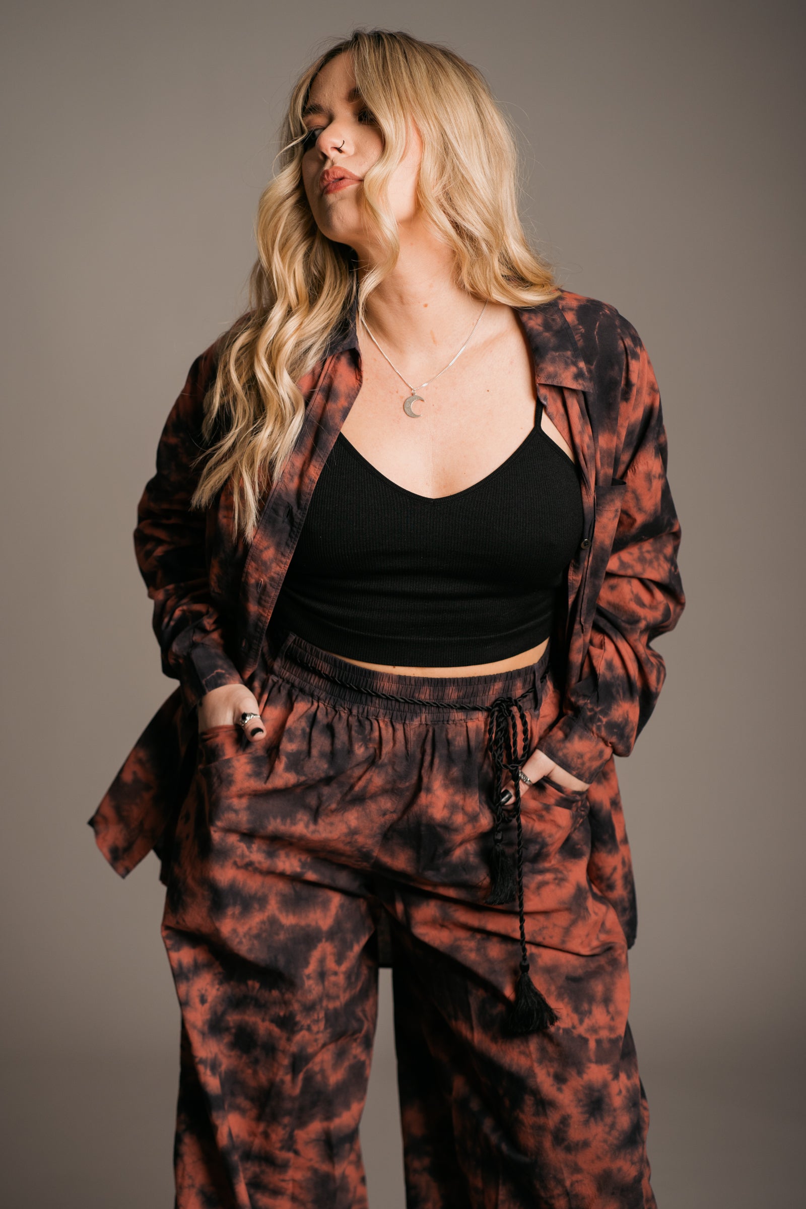 Model Erin wearing the Little Lies Zephyr Tie Dye Co-Ord, a vibrant tie-dye co-ord set featuring a relaxed-fit long-sleeve shirt worn open and matching wide-leg, tie-waist trousers. Styled with ankle-tie black sandals, the look embodies effortless bohemian style against a neutral backdrop.