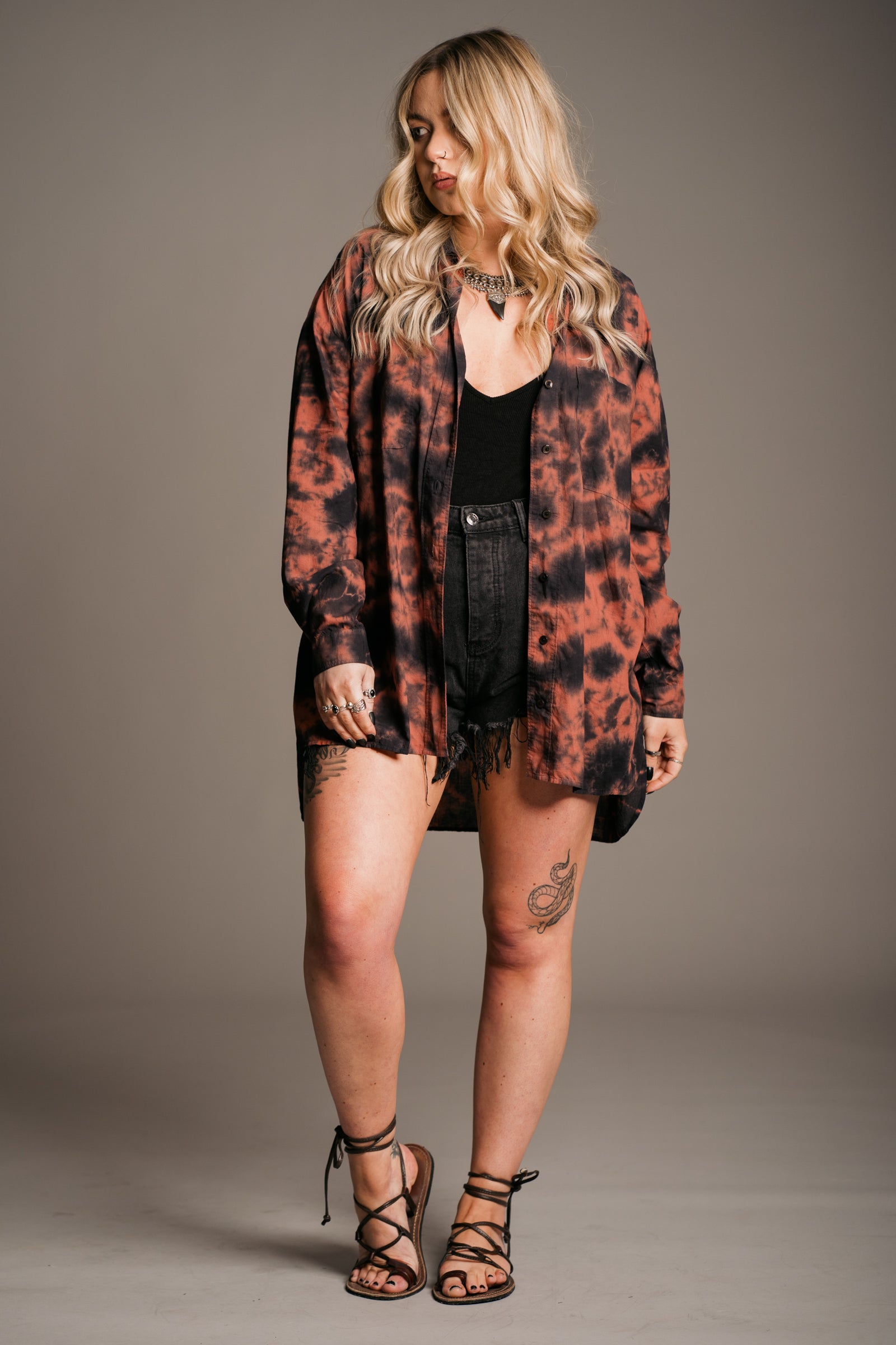 Model Erin wearing the Little Lies Zephyr Tie Dye Co-Ord Shirt, a vibrant tie-dye co-ord set featuring a relaxed-fit long-sleeve shirt. Styled with vintage distressed Levi's denim shorts, black vest top and ankle-tie black sandals, the look embodies effortless bohemian style against a neutral backdrop.