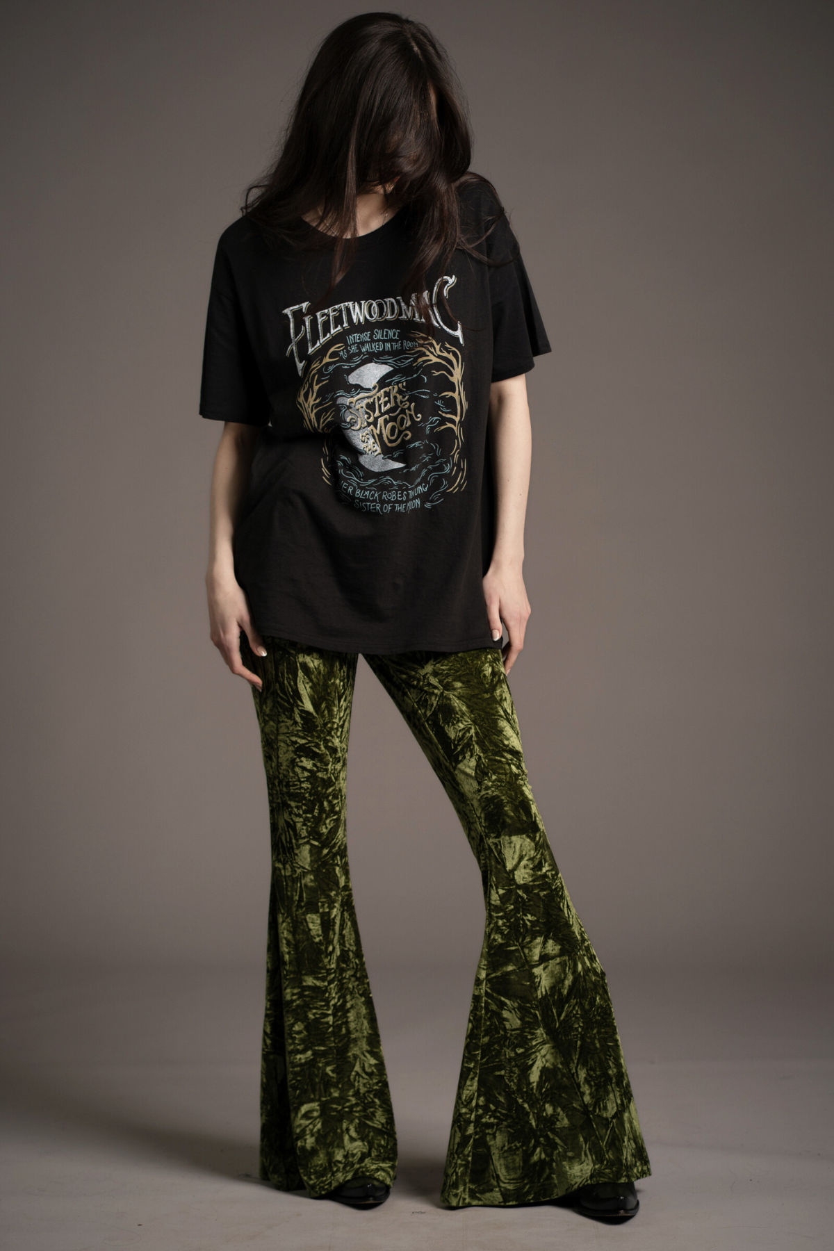 Andie models Little Lies Hendrix olive crushed velvet flared trousers with dramatic bell-bottom silhouette, styled with oversized Fleetwood Mac graphic tee and black ankle boots in studio setting