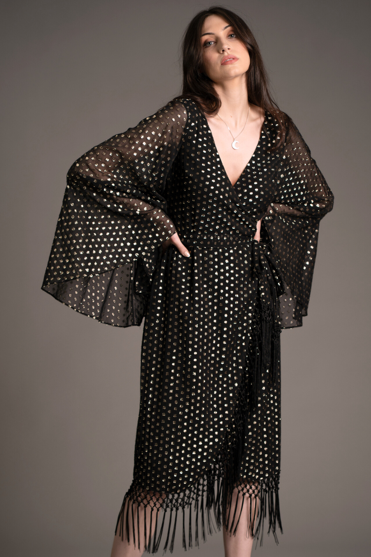 Andie models Little Lies Cosmic Dancer metallic wrap dress with gold foil polka dot pattern, sheer bell sleeves, and tassel hem