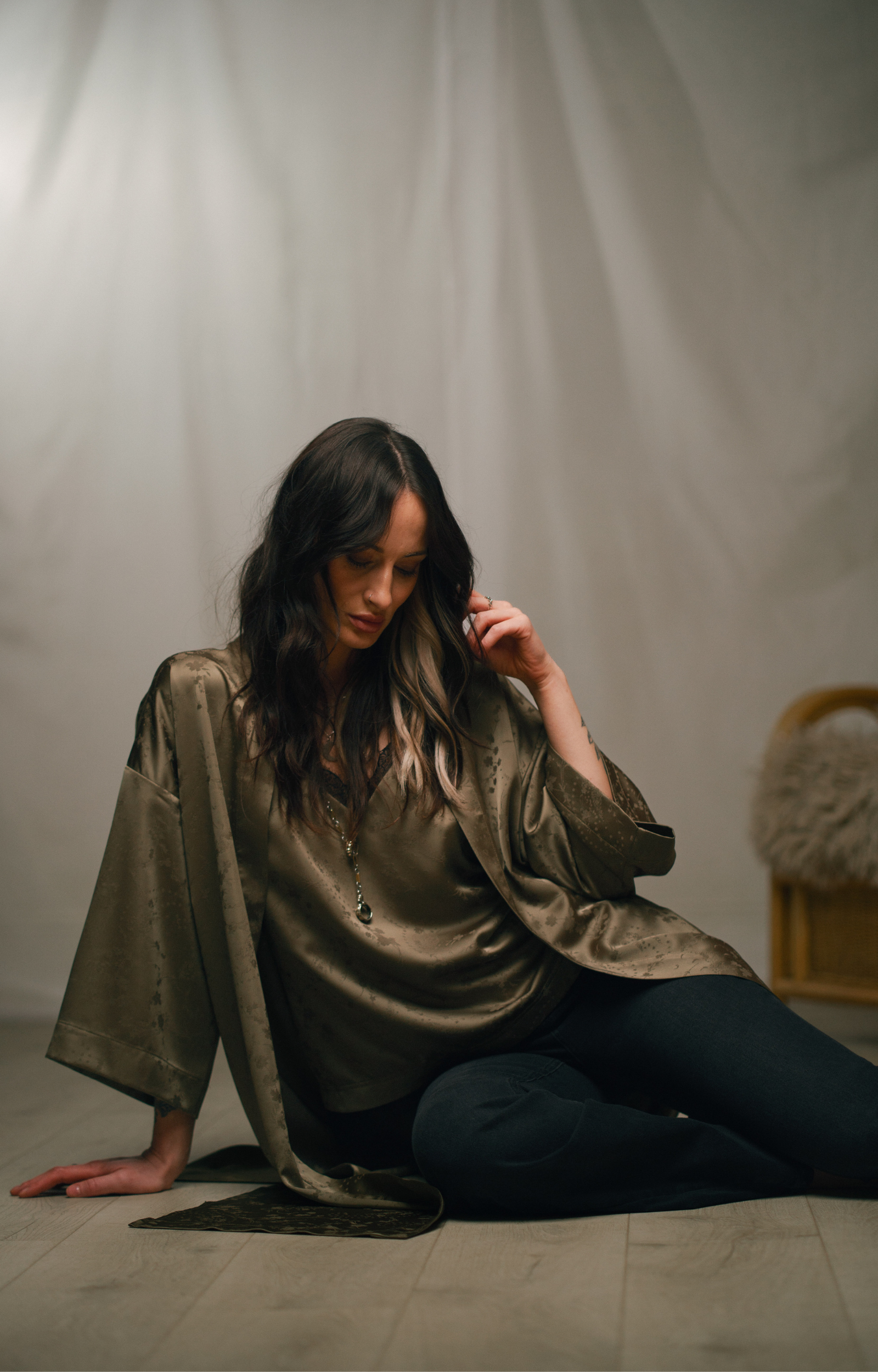 Front view of Victoria wearing the Little Lies Iris Satin Kimono in olive satin with a subtle floral jacquard pattern, layered over a matching Iris Satin Cami and styled with denim flared trousers.