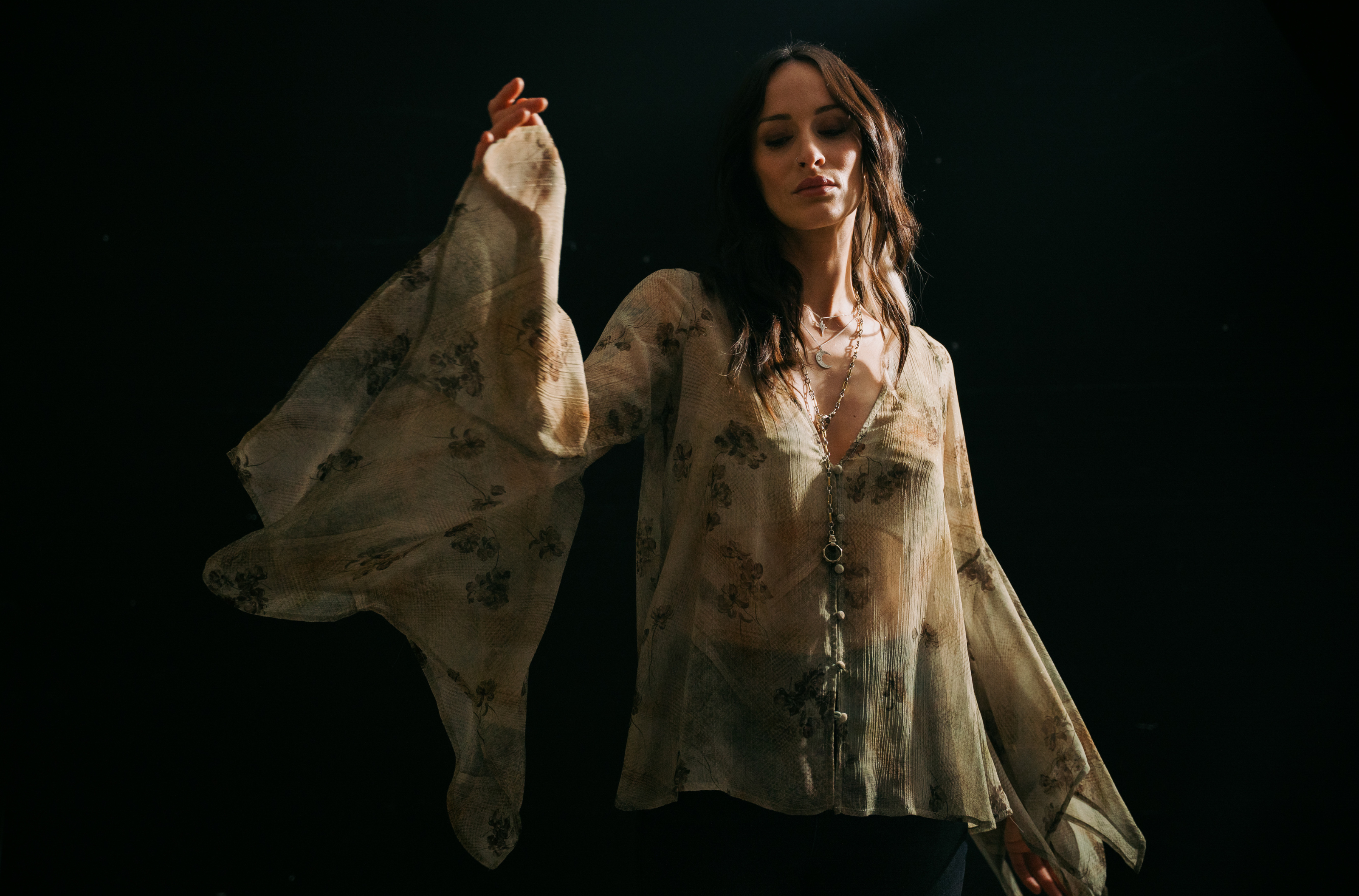 Wearing the Little Lies Karma Sage Blouse in soft sage floral print with flowing asymmetric sleeves.