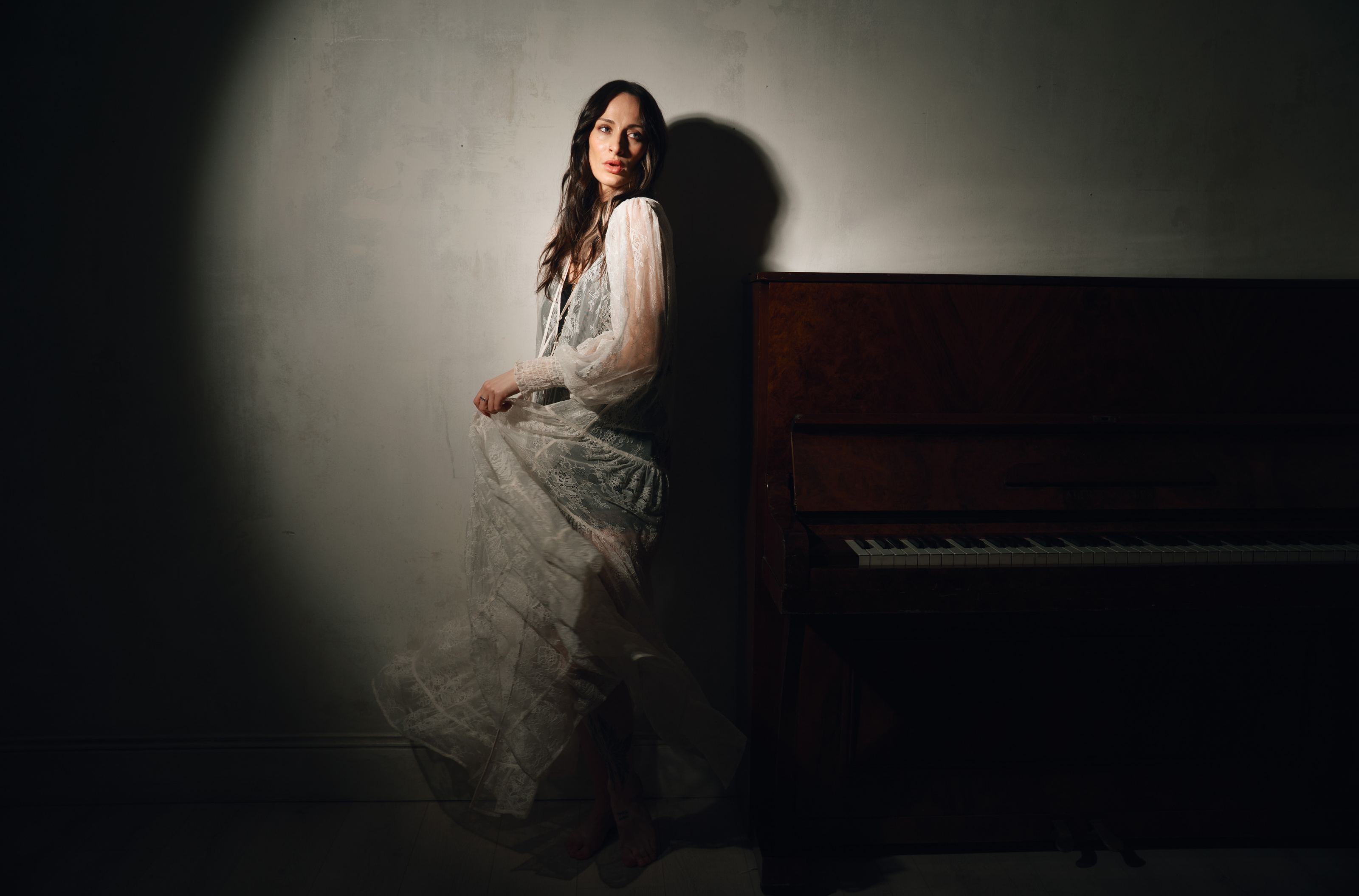 Model wearing the Little Lies Rhiannon Ivory Maxi Dress featuring sheer ivory lace fabric, long voluminous sleeves, tassel ties, and a tiered maxi‑length skirt worn over the Nightbird Satin Slip Dress as an underlayer.