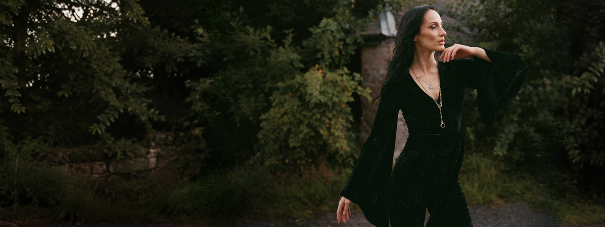 Model wearing the Little Lies Sally Black Velvet Wrap Top with dramatic bell sleeves in an outdoor Spellbound campaign shoot.