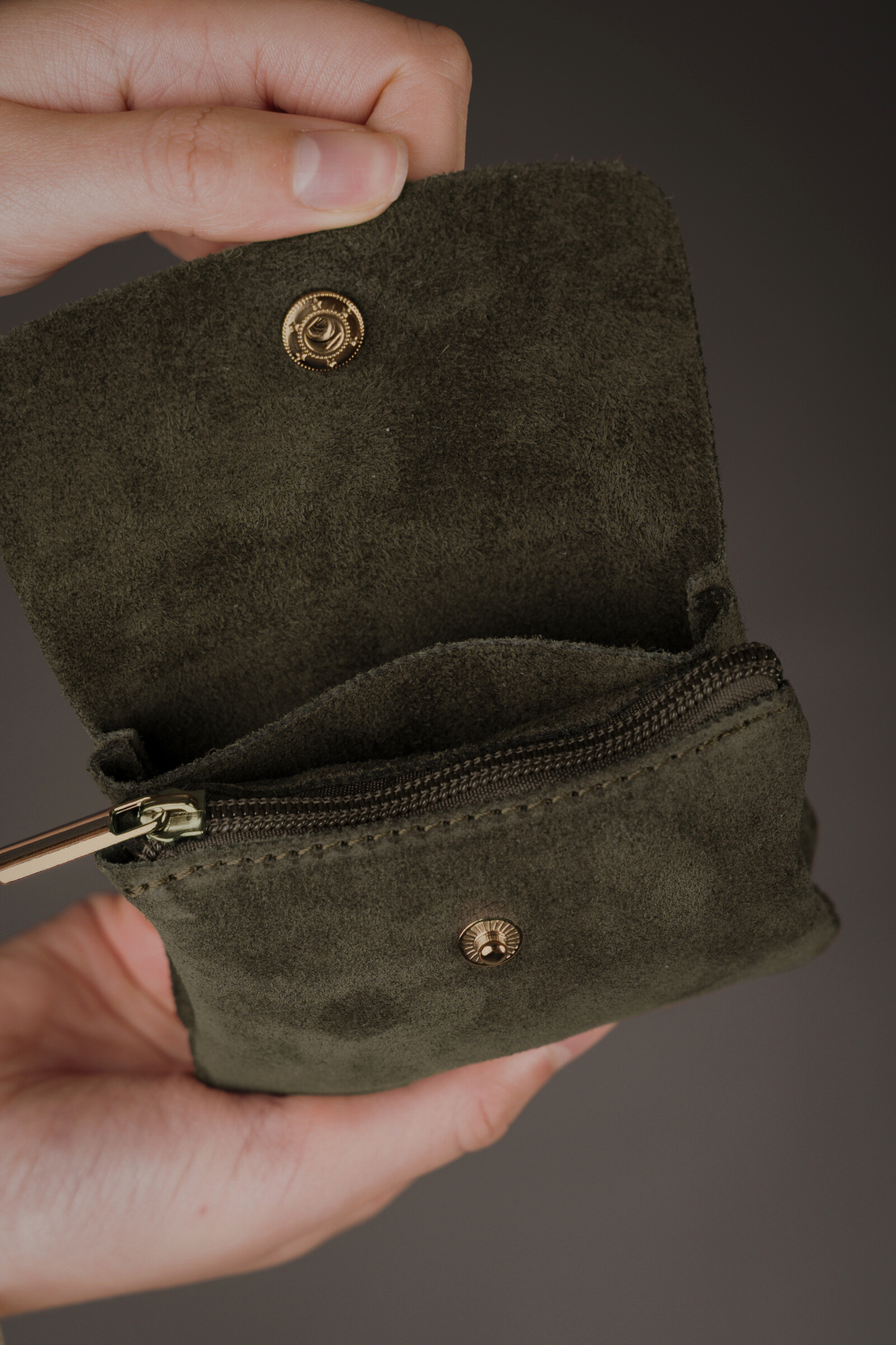 Open khaki genuine suede purse showing zip compartment and gold snap button, held against a grey background.
