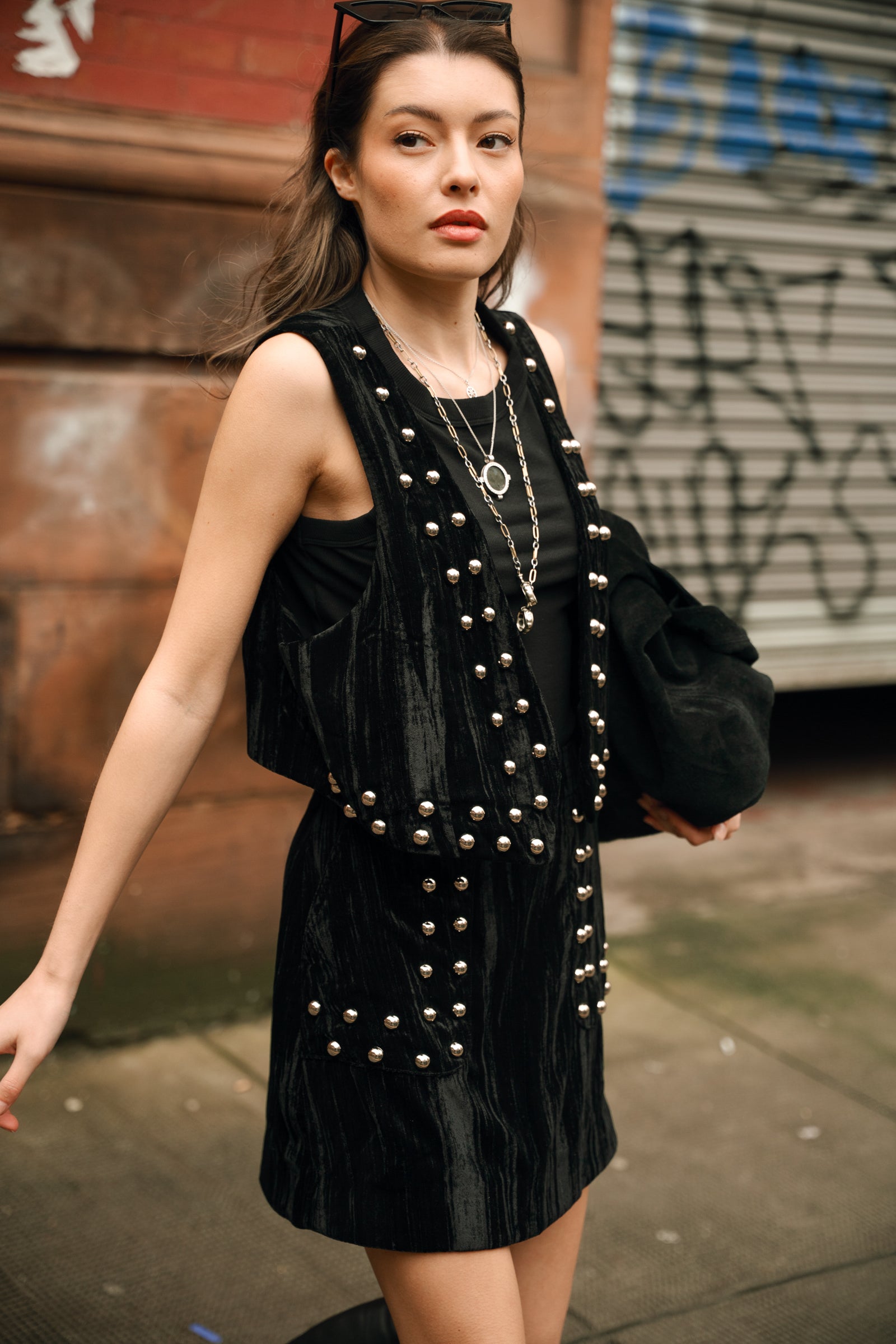 Model wearing Little Lies Lennon studded velvet mini skirt styled with black top, matching waistcoat and knee-high boots for edgy street-style outfit