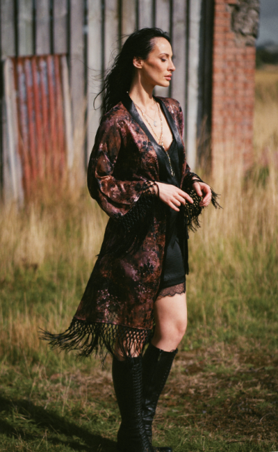 Model wearing the Little Lies Practical Magic Kimono in a Spellbound collection campaign shoot, featuring a celestial-inspired print and statement fringe detailing styled over a black lace slip dress.