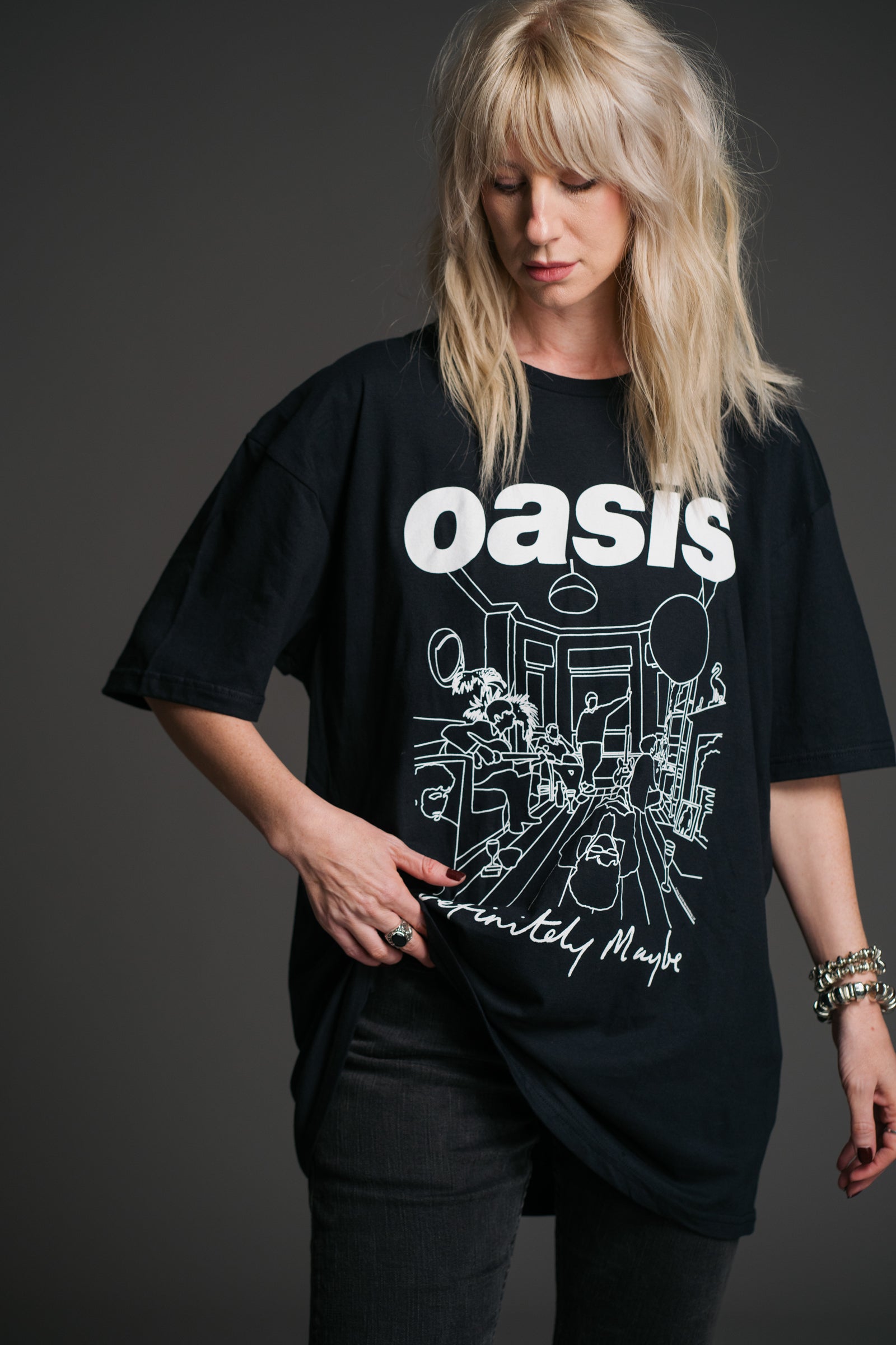 Sara wears unisex black Oasis Definitely Maybe graphic band t‑shirt by Little Lies featuring bold white Oasis logo and album‑inspired line‑art design.