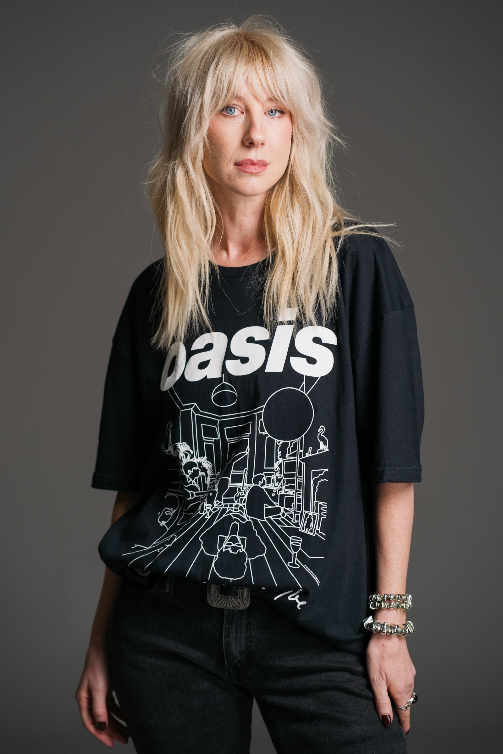 Sara wears unisex black Oasis Definitely Maybe graphic band t‑shirt by Little Lies featuring bold white Oasis logo and album‑inspired line‑art design.