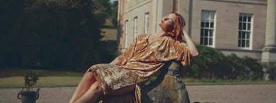 Anna in Rumours Ochre Velvet dress sitting on a stone dog statue at the Byre at Inchyra.