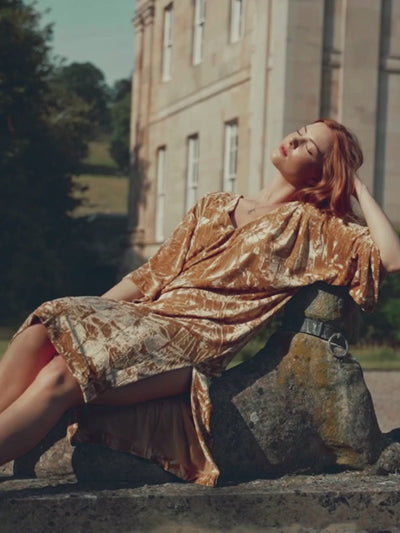 Anna in Rumours Ochre Velvet dress sitting on a stone dog statue at the Byre at Inchyra.
