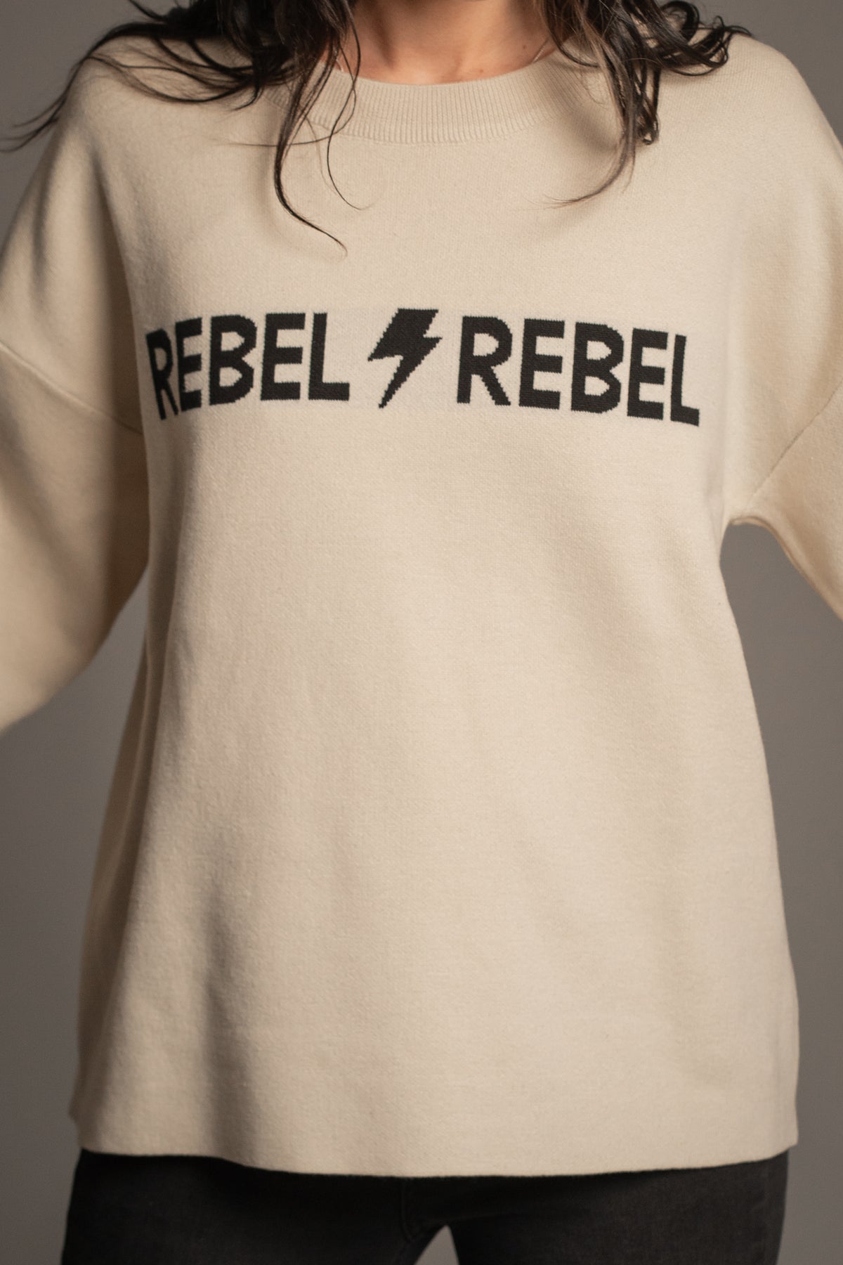 Close-up of Rebel Rebel Cream Knit Jumper showing black REBEL REBEL slogan and lightning bolt graphic