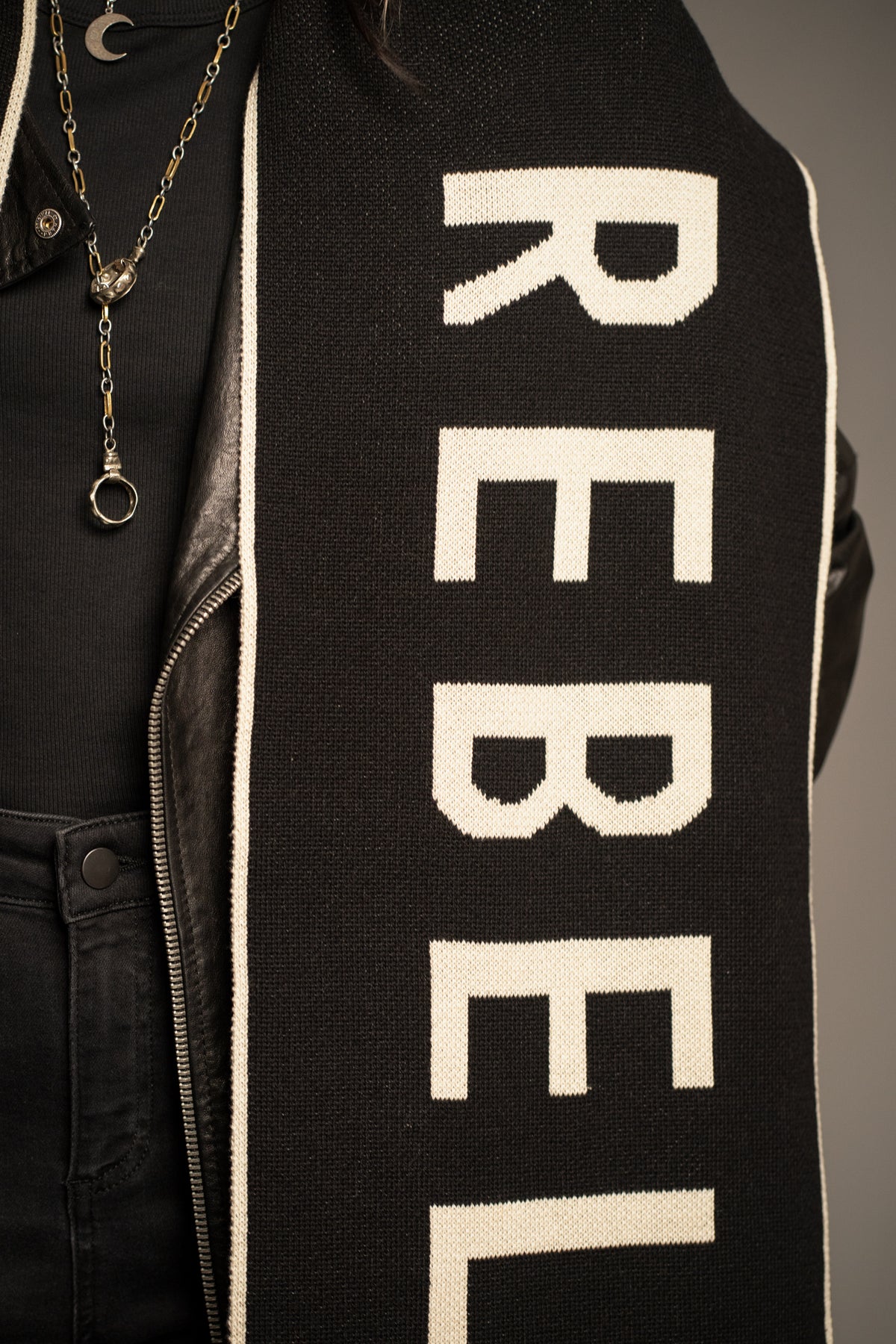 Detail view of the Rebel Rebel Knit Scarf showcasing bold ivory lettering on soft black knit fabric