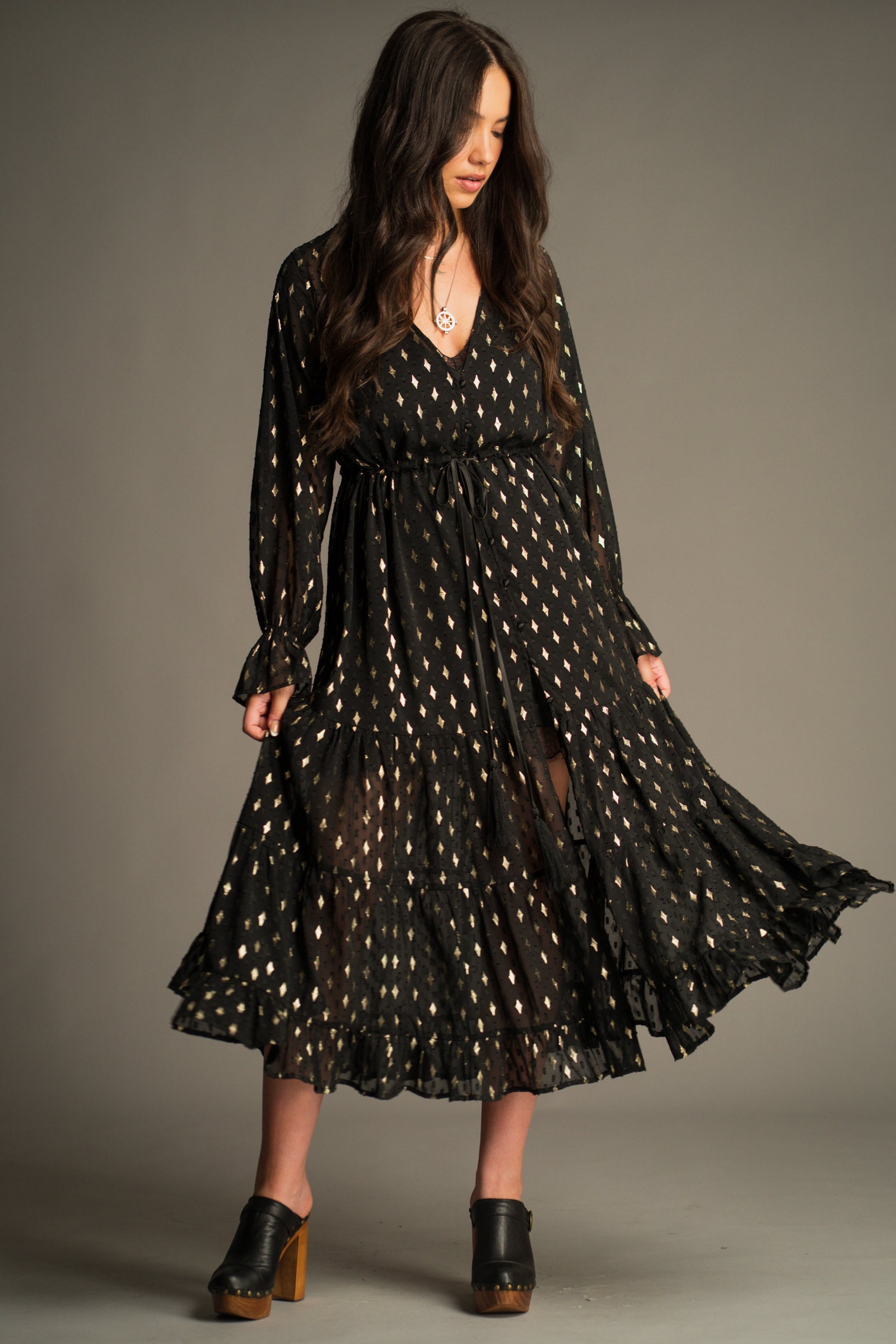 Front view of the Space Oddity Metallic Maxi Dress featuring a sheer black overlay, metallic gold foil print, drawstring waist and tiered maxi silhouette