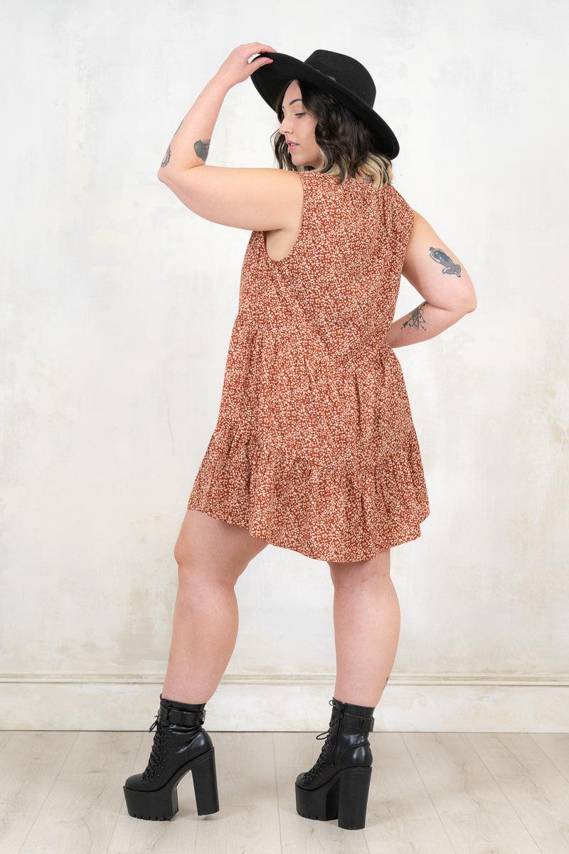 Model wearing Landslide Rust Smock - Rust and cream ditsy floral print, sleeveless smock dress with a tiered a-line skirt and plunge neckline