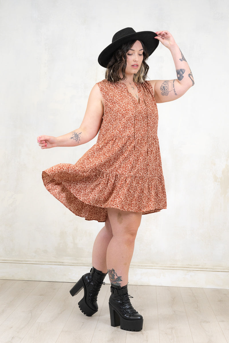 Model wearing Landslide Rust Smock - Rust and cream ditsy floral print, sleeveless smock dress with a tiered a-line skirt and plunge neckline