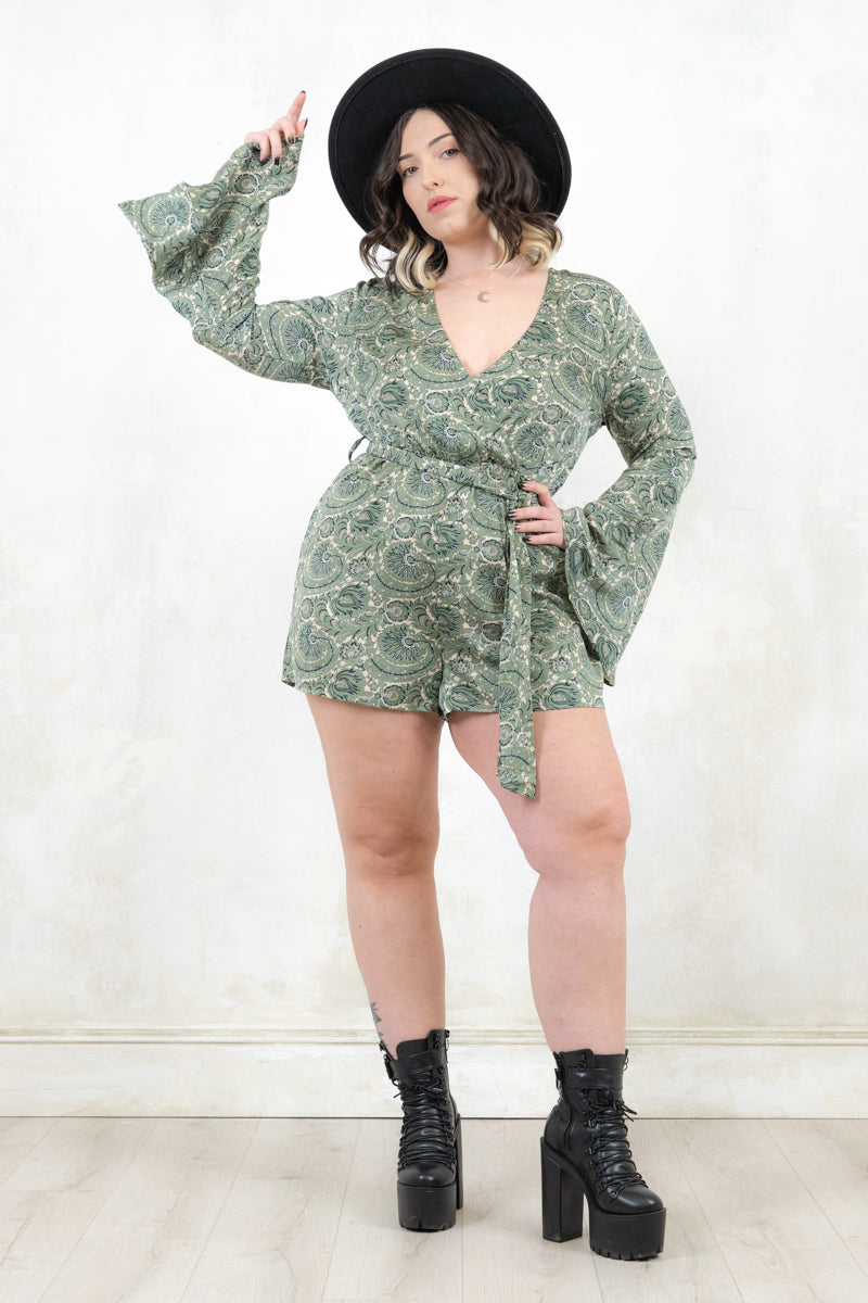Model wearing Secret Garden Playsuit, a green paisley print jumpsuit with an Elasticated waist, fixed wrap front with v-neckline, flared cuff, concealed zip at back