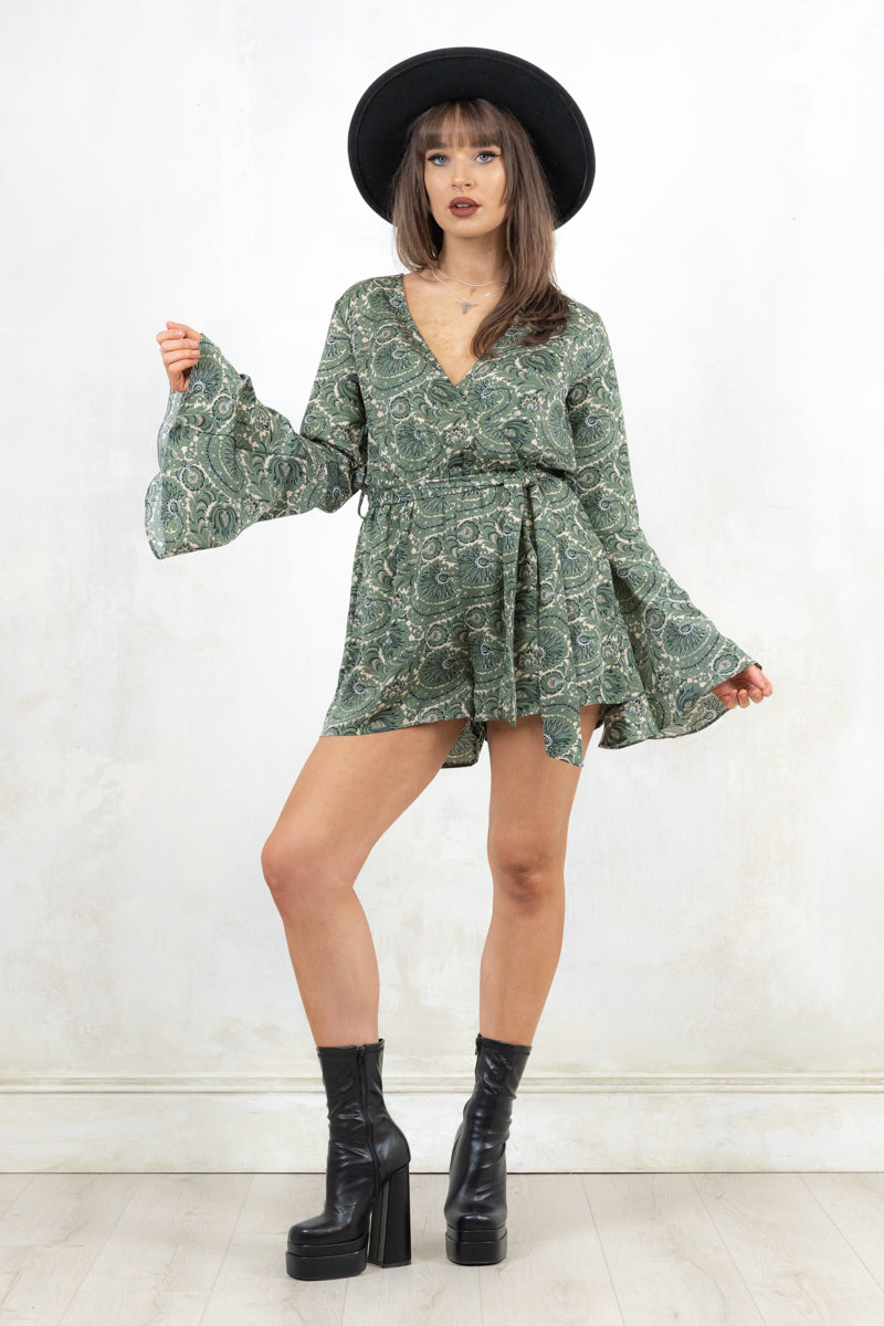 Model wearing Secret Garden Playsuit, a green paisley print jumpsuit with an Elasticated waist, fixed wrap front with v-neckline, flared cuff, concealed zip at back